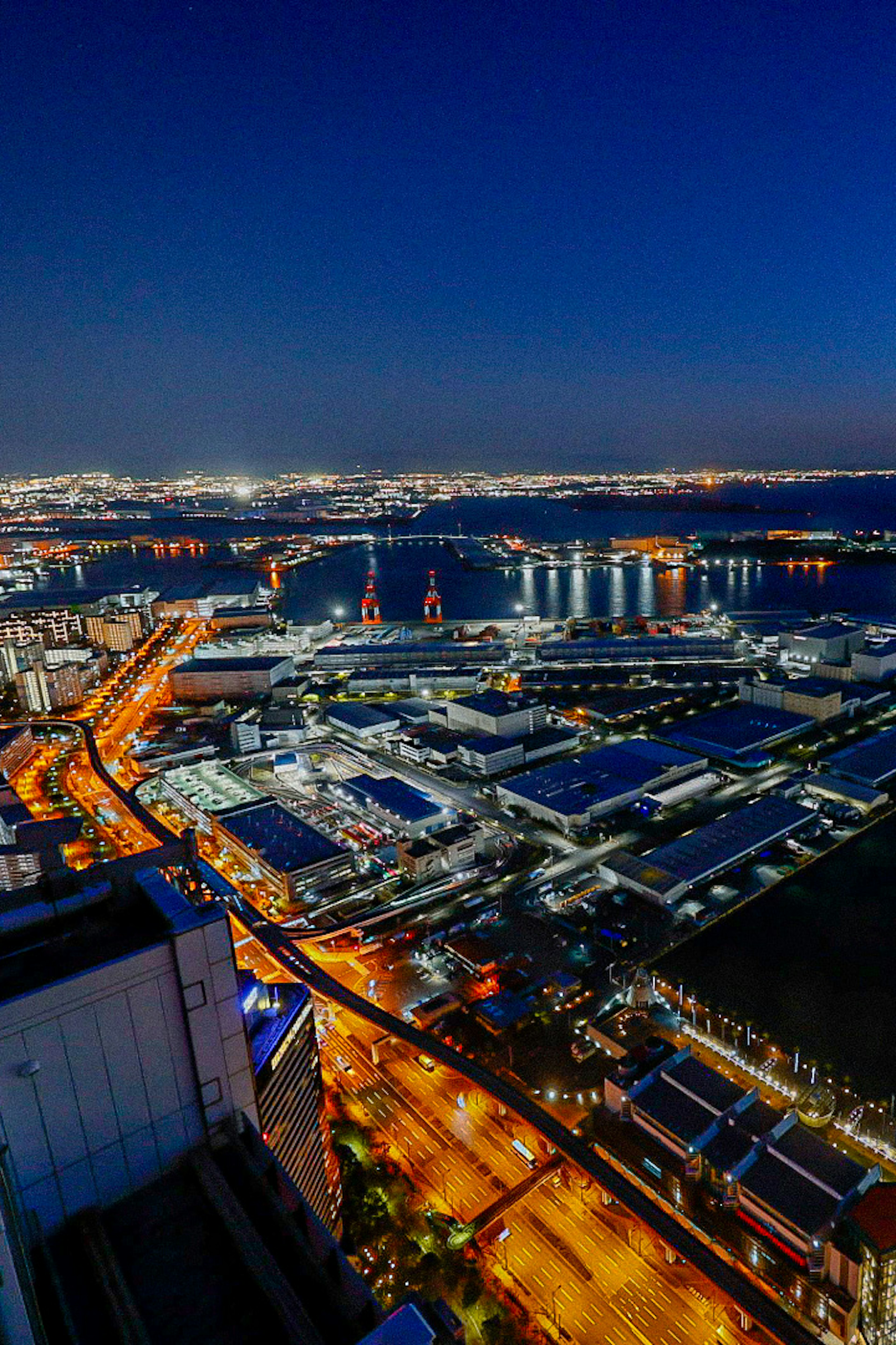 Vue panoramique d'une ville la nuit avec des lampadaires lumineux et des zones industrielles se reflétant sur l'eau du port