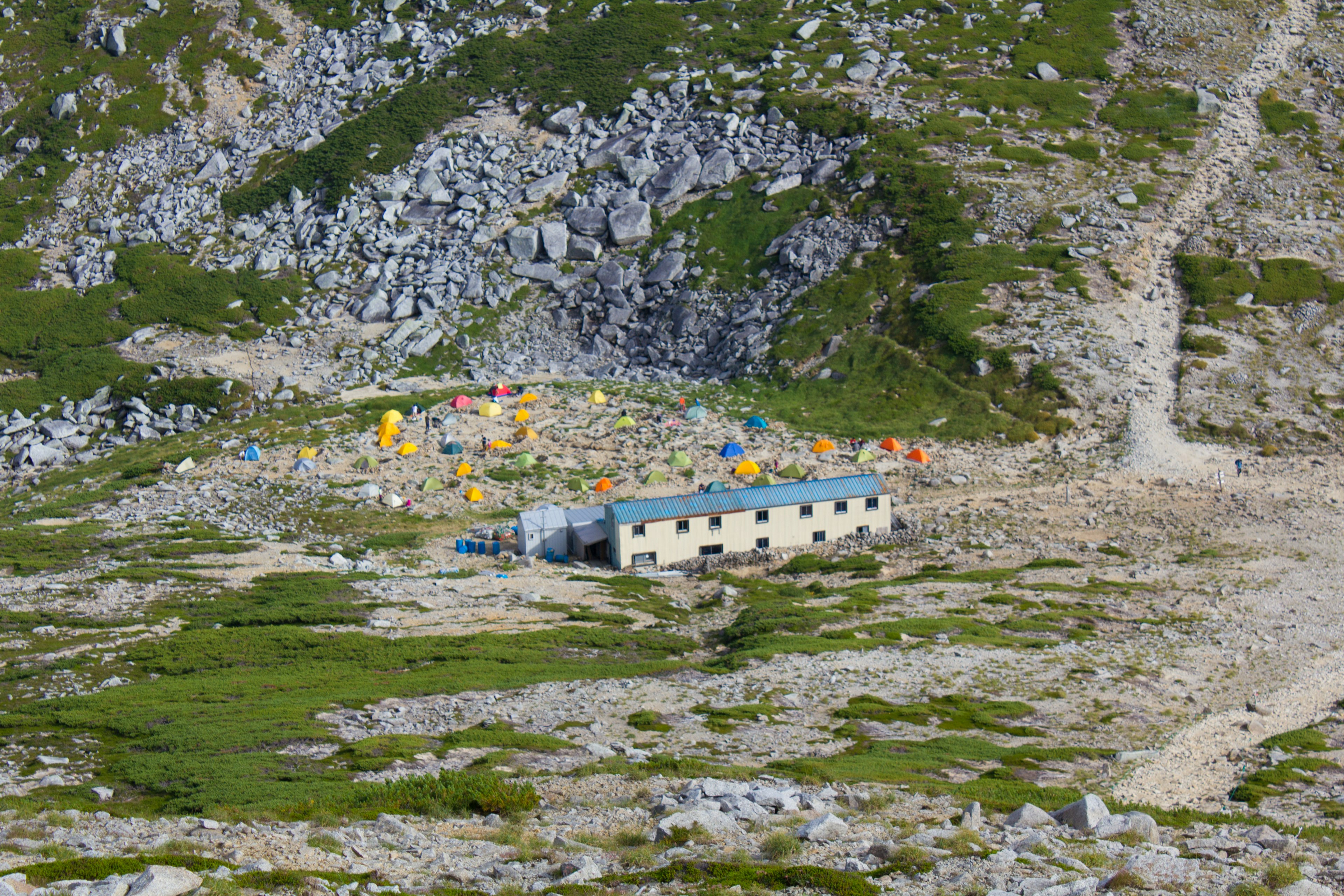 Kleines Gebäude und bunte Zelte in einer bergigen Landschaft