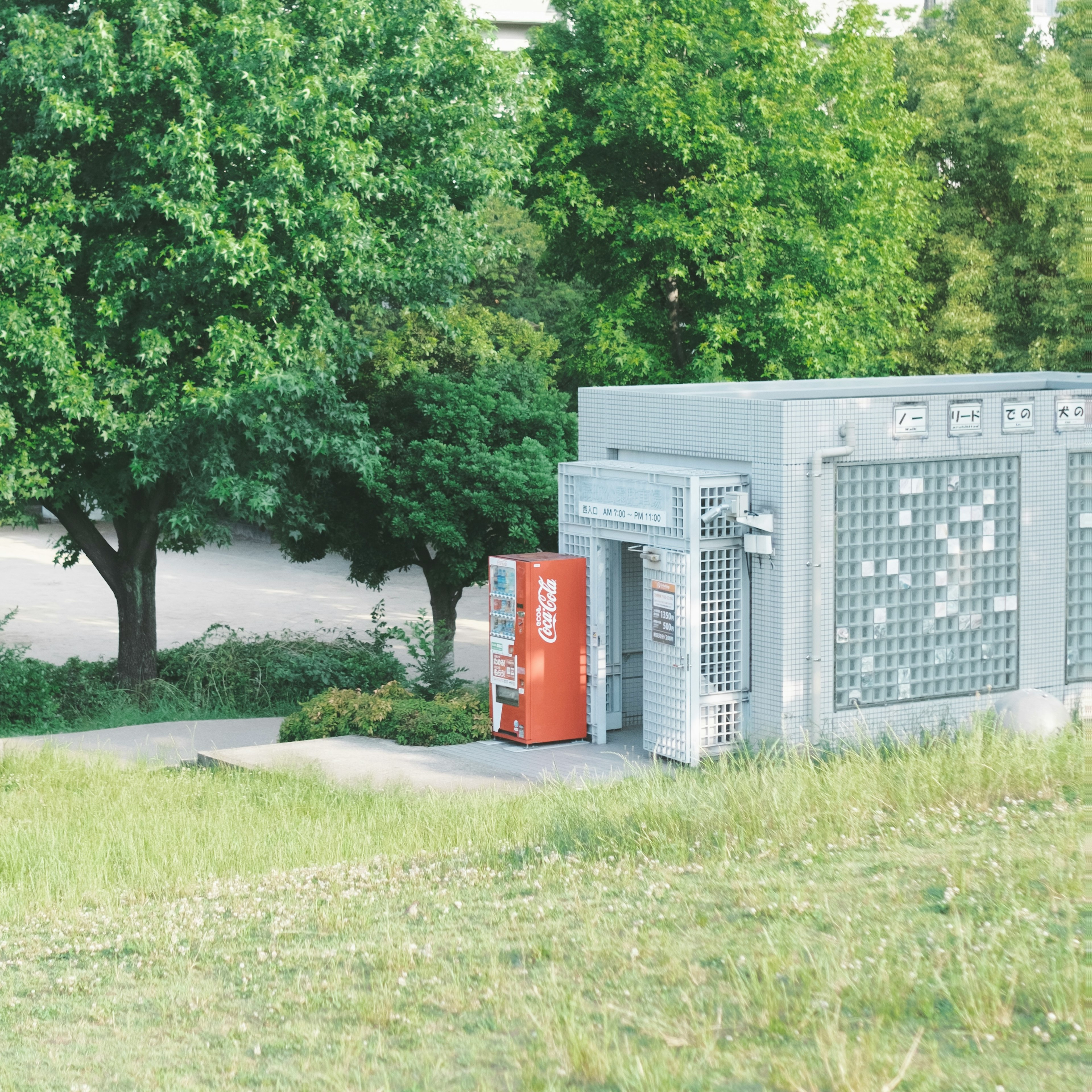 緑の木々の前にある自販機と灰色の建物