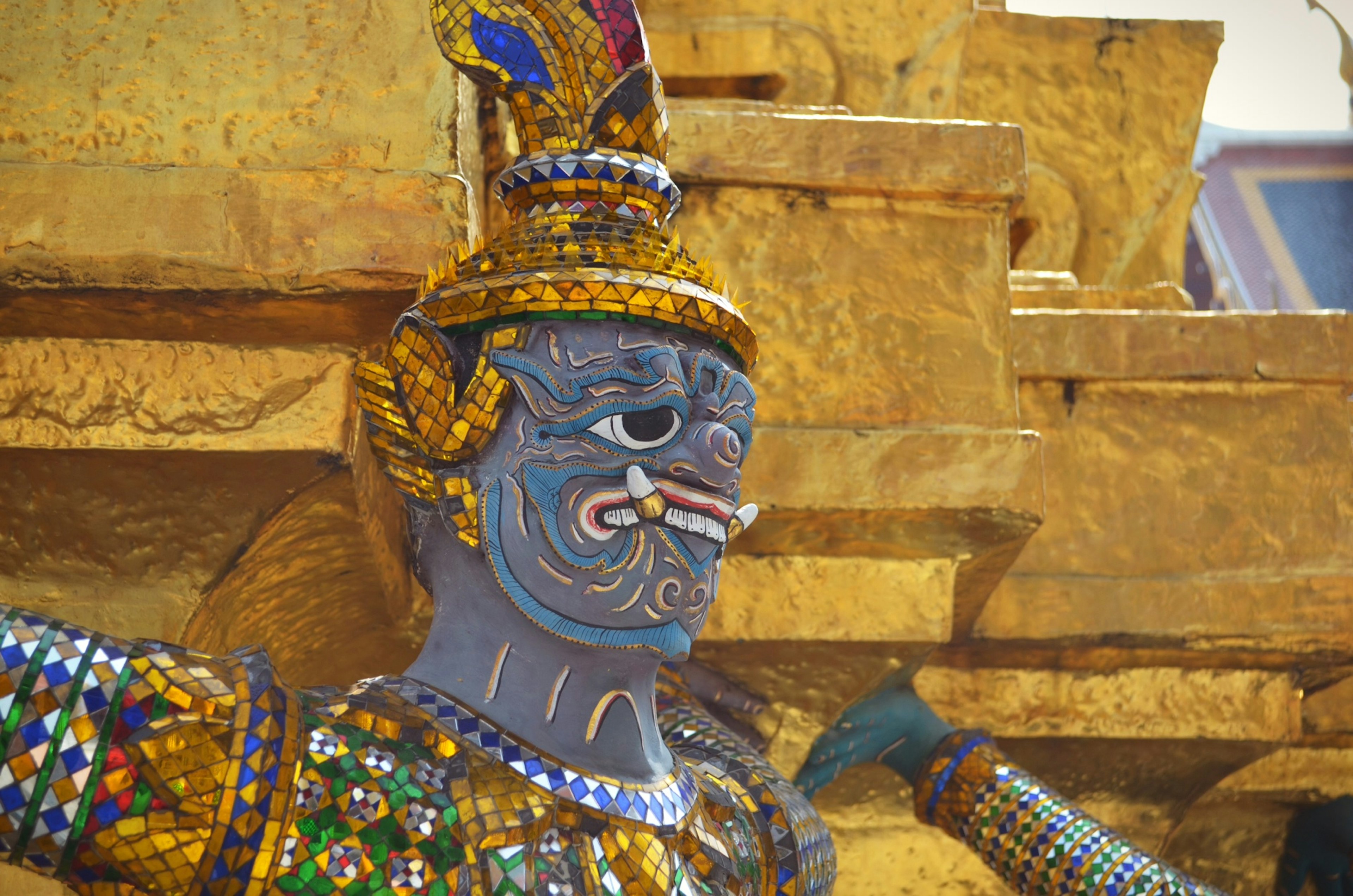 Statue with blue skin adorned in colorful decorations against a golden background