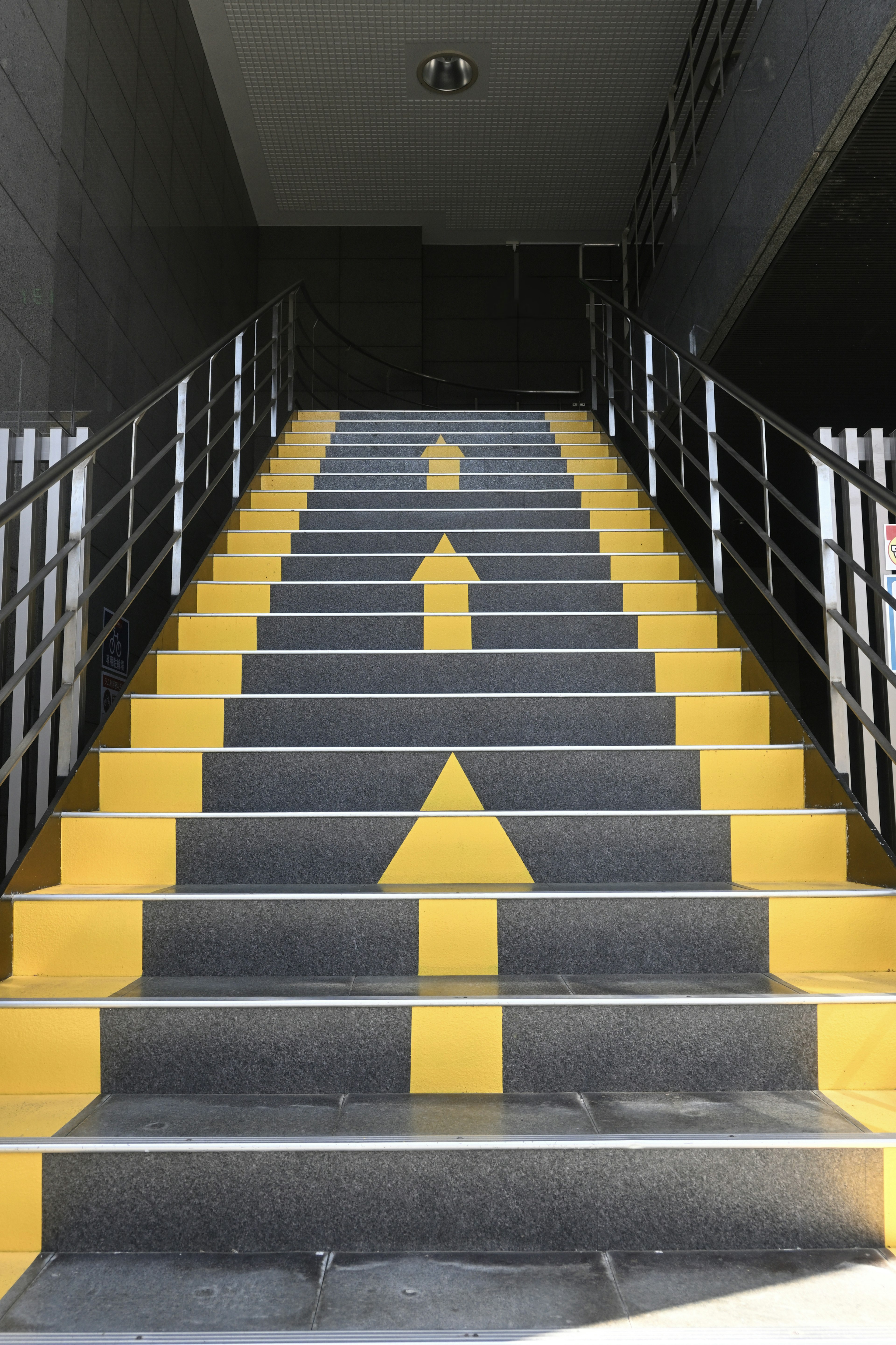 Escalier avec des flèches jaunes pointant vers le haut sur des marches noires