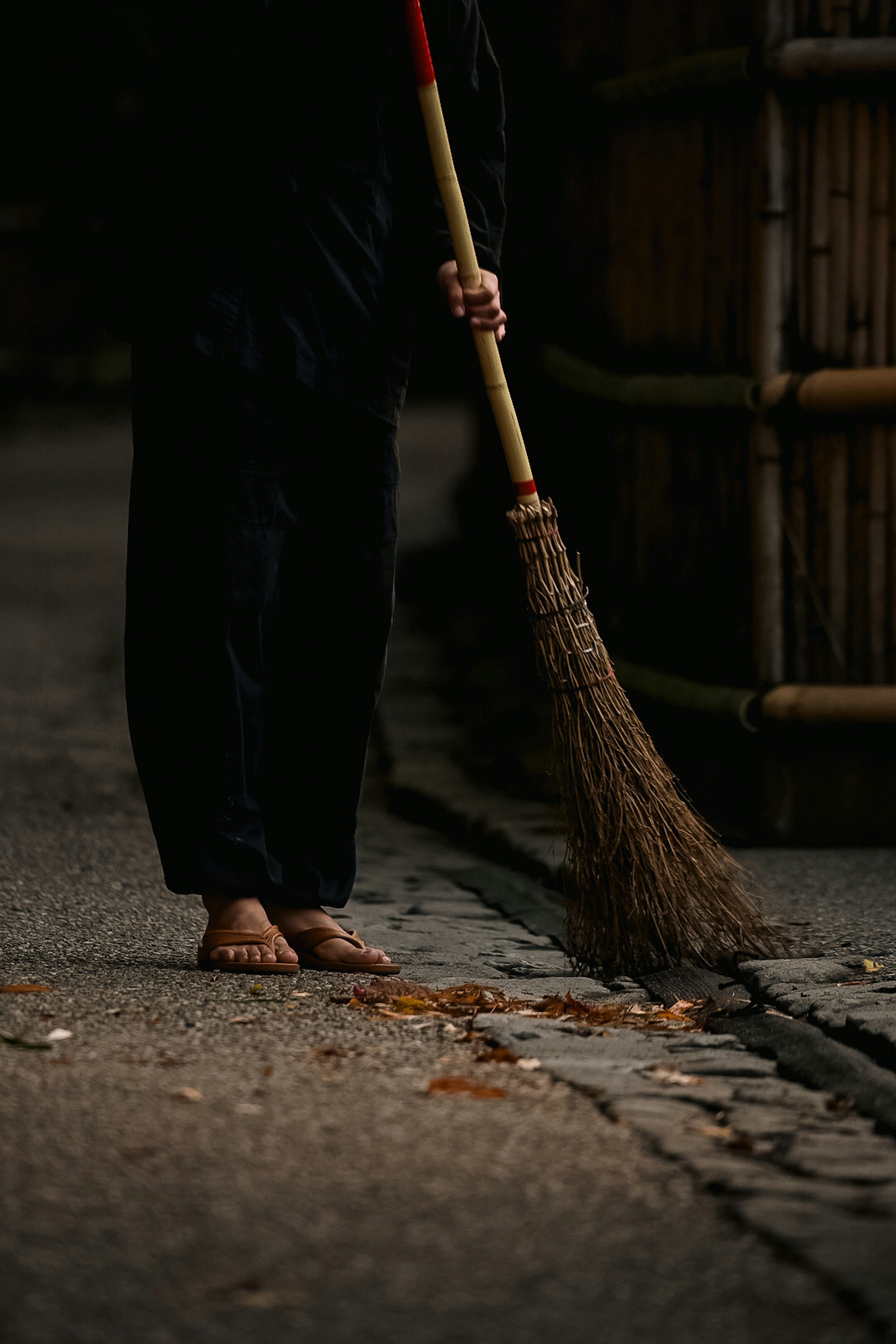 Barefoot person sweeping near a bamboo fence