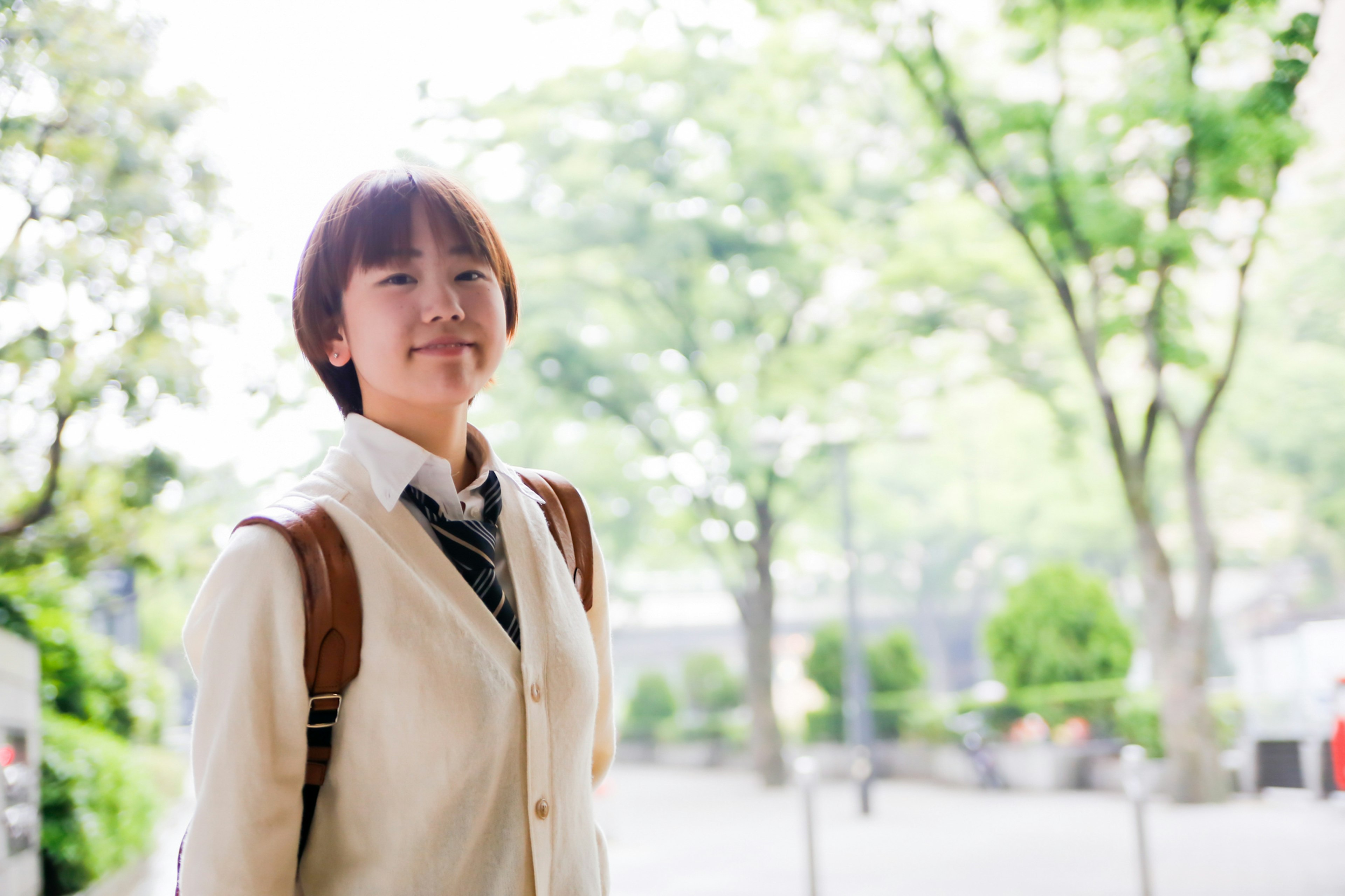 Woman smiling in a park with trees wearing a white jacket and carrying a backpack