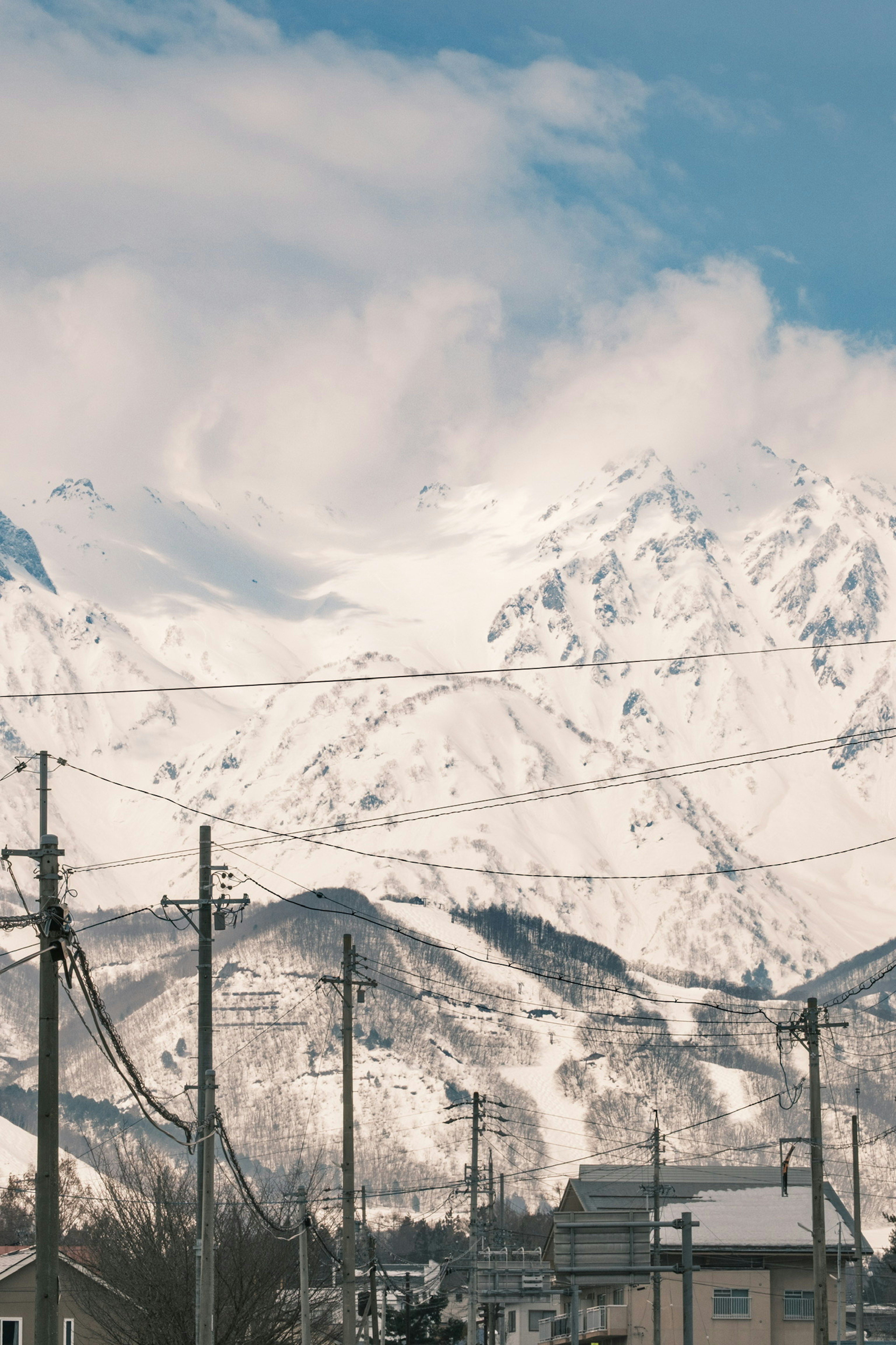 雪覆蓋的山脈在藍天之下，前景有電線和建築物