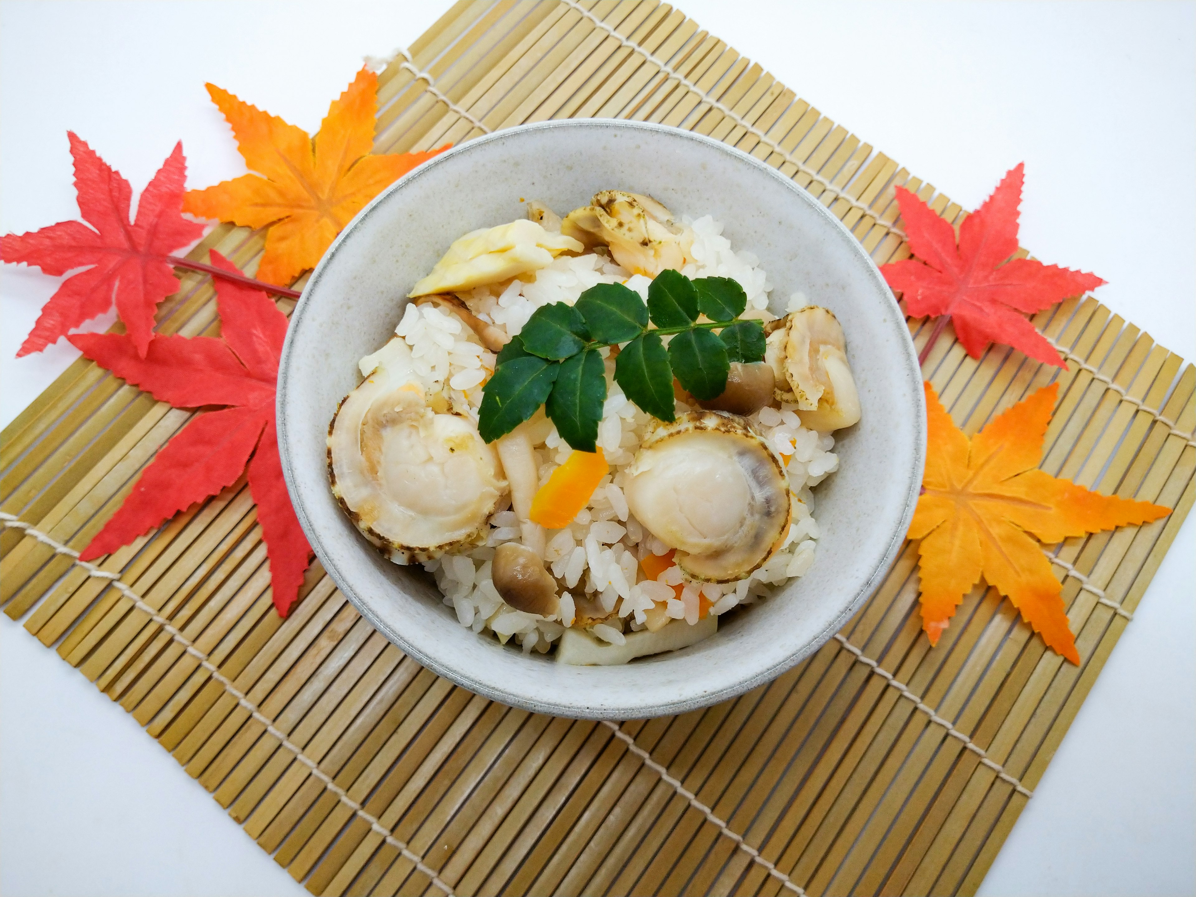 Tazón de arroz cubierto con mariscos y verduras rodeado de hojas de otoño