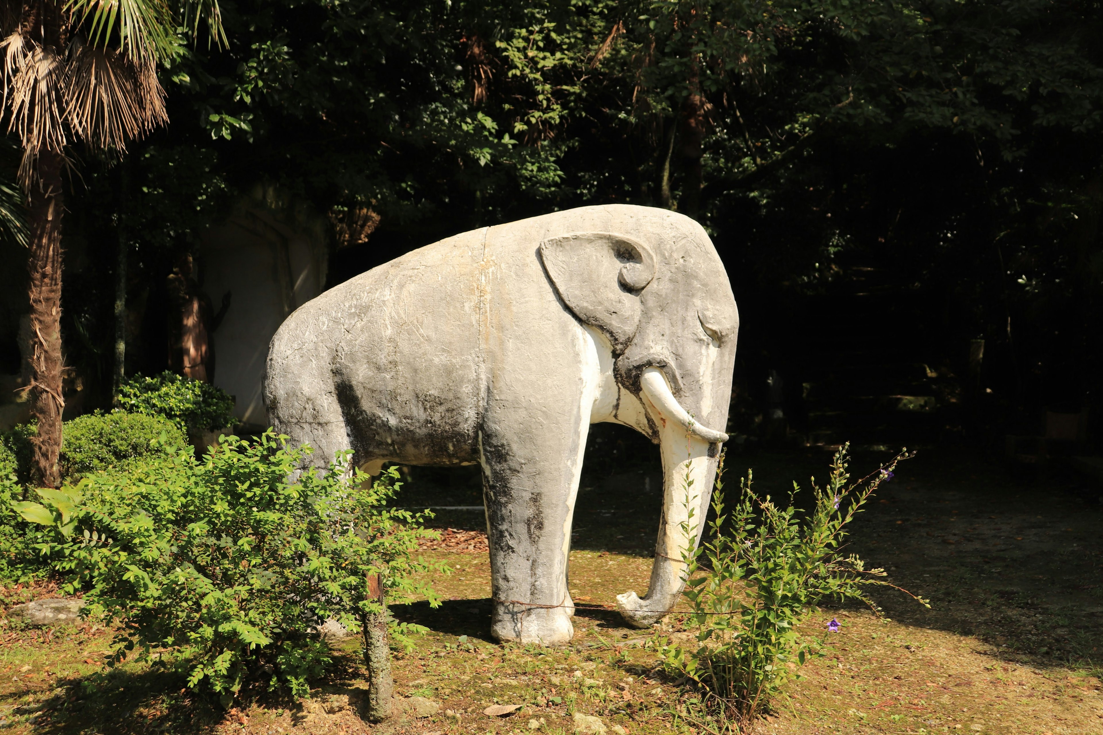 Weißer Elefantenskulptur steht in einem Garten umgeben von grünen Pflanzen