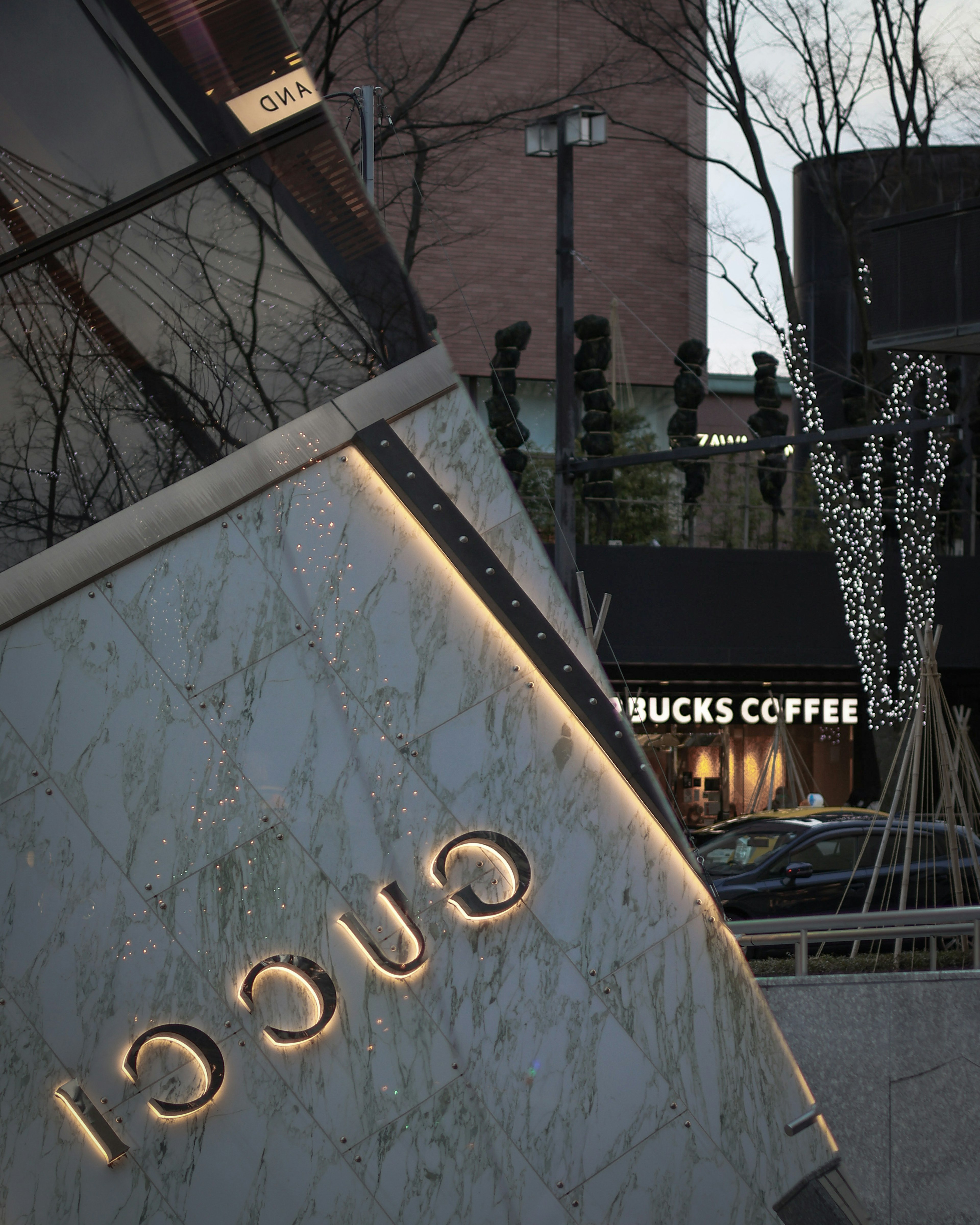 Logo iluminado de Gucci en un letrero de mármol con una tienda Starbucks al fondo