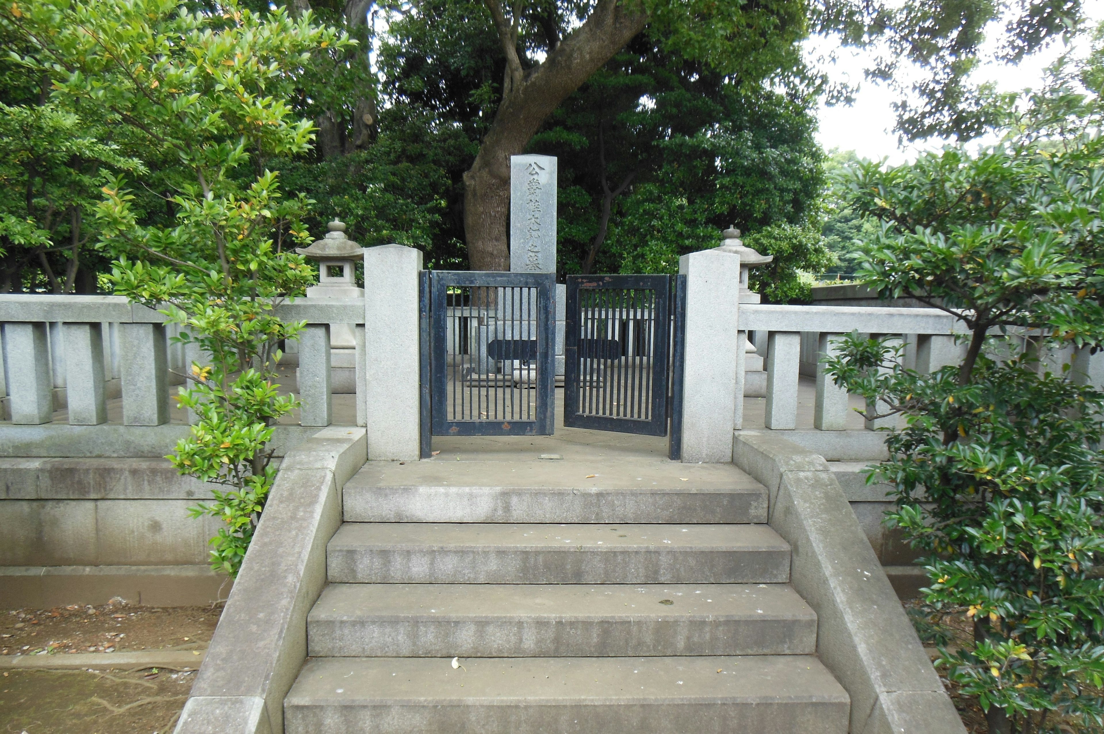 Garden entrance with stairs and black gate surrounded by green trees