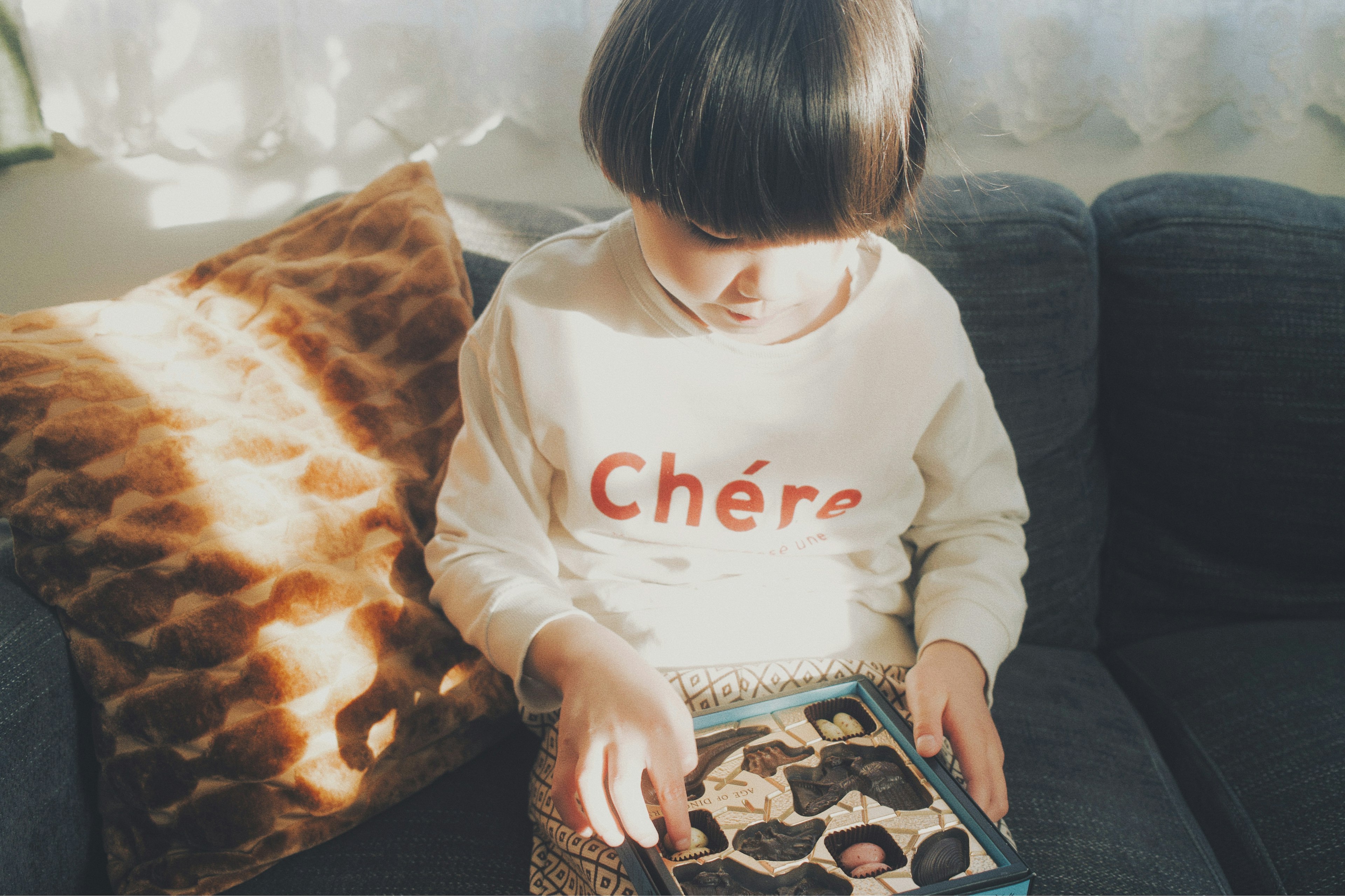 Anak yang duduk di sofa dengan bantal coklat sambil melihat foto