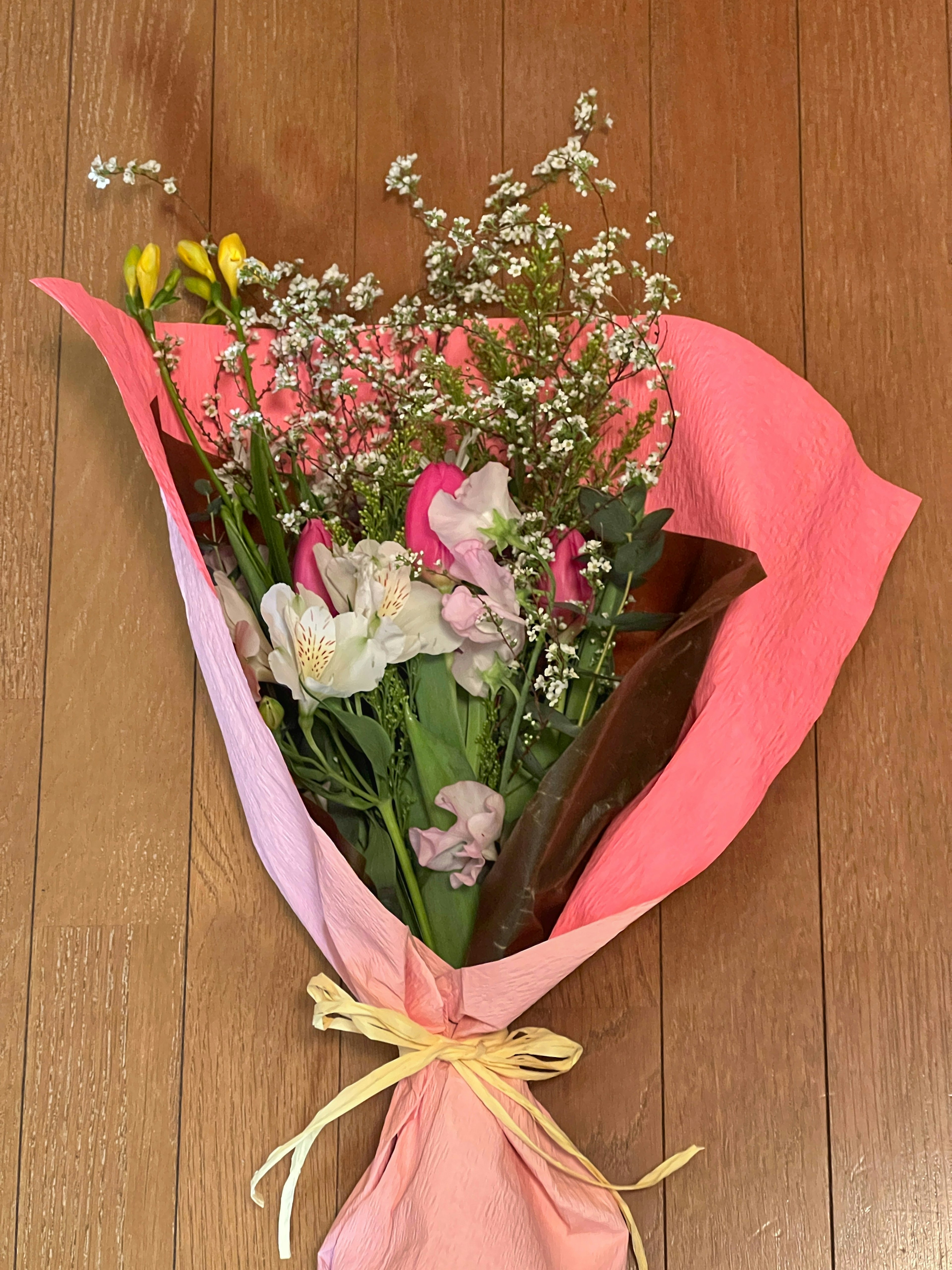 Bouquet wrapped in pink and orange paper featuring various colorful flowers and delicate baby’s breath