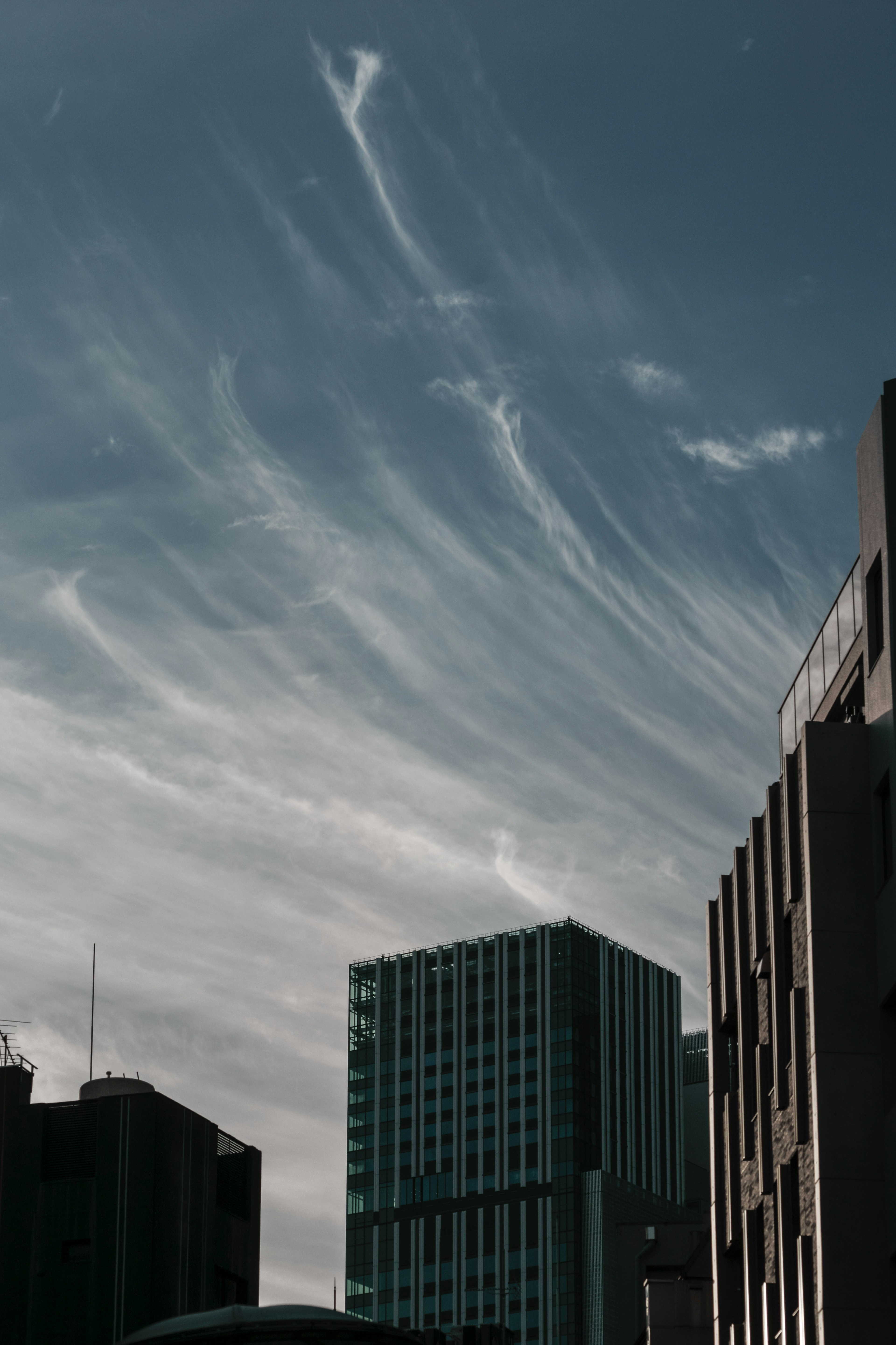 Silhouette de bâtiments contre un ciel bleu avec des nuages filamenteux