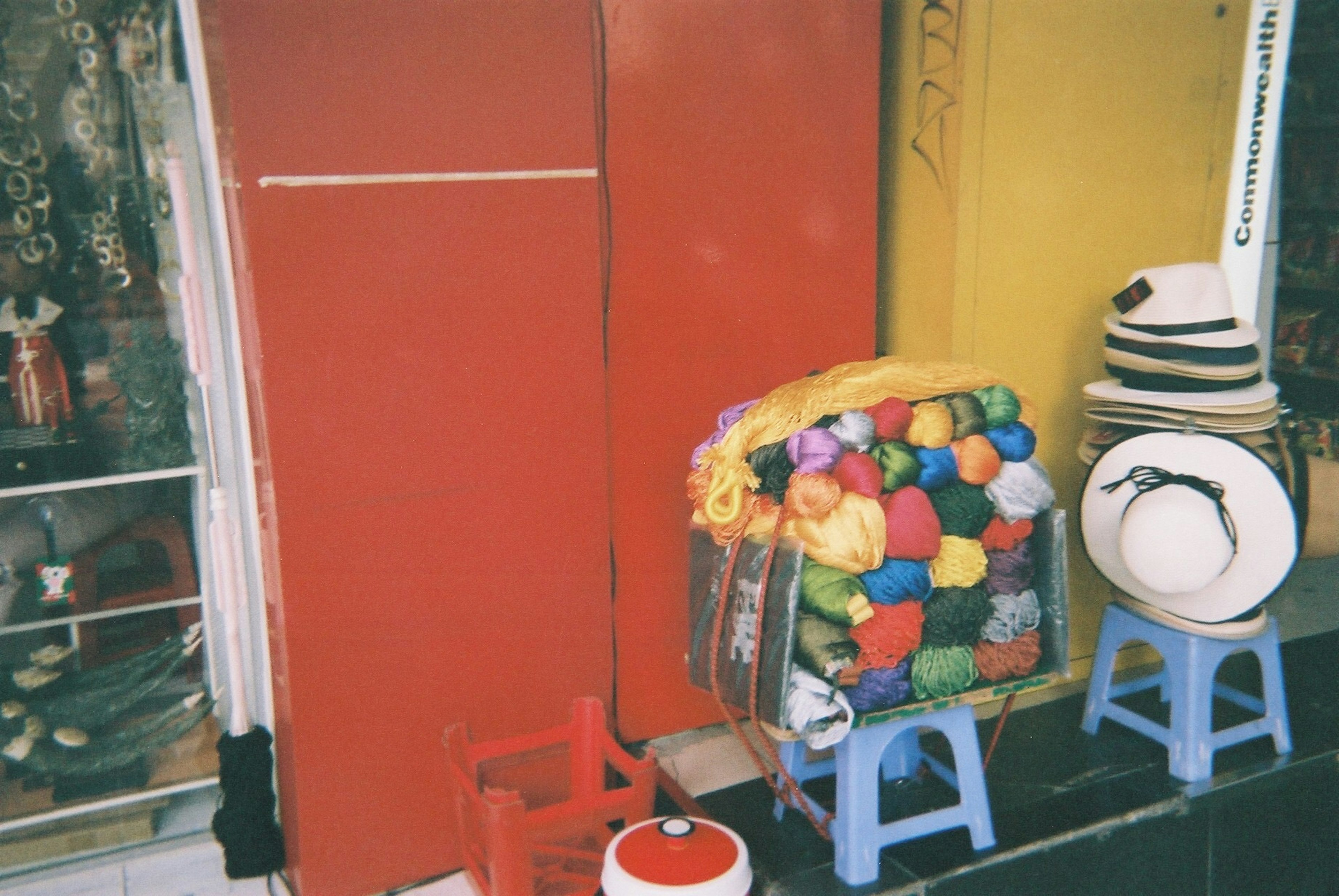 A vibrant display of colorful yarn balls next to a red door with hats on stools