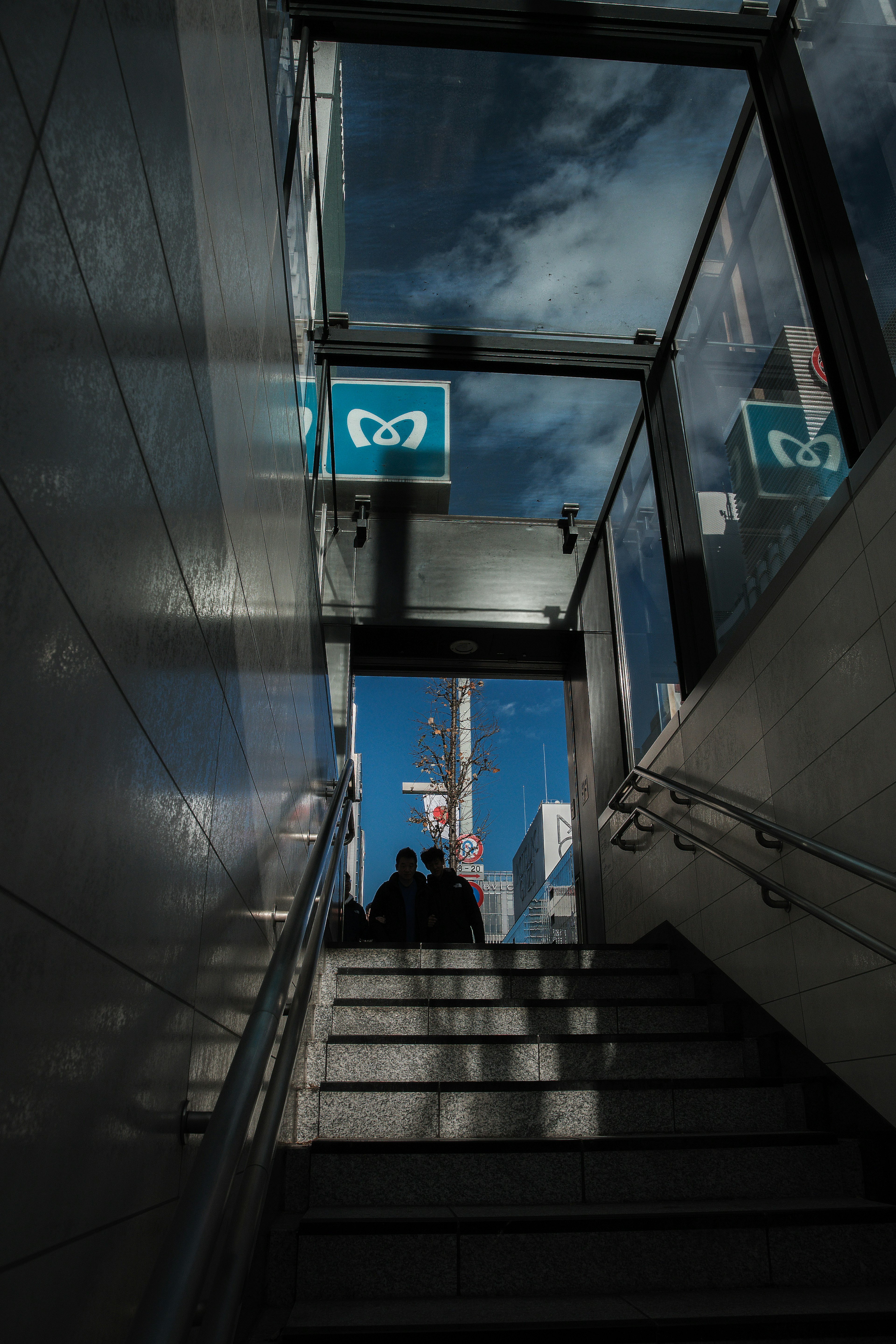 View from the bottom of stairs with silhouettes and glass walls reflecting blue sky