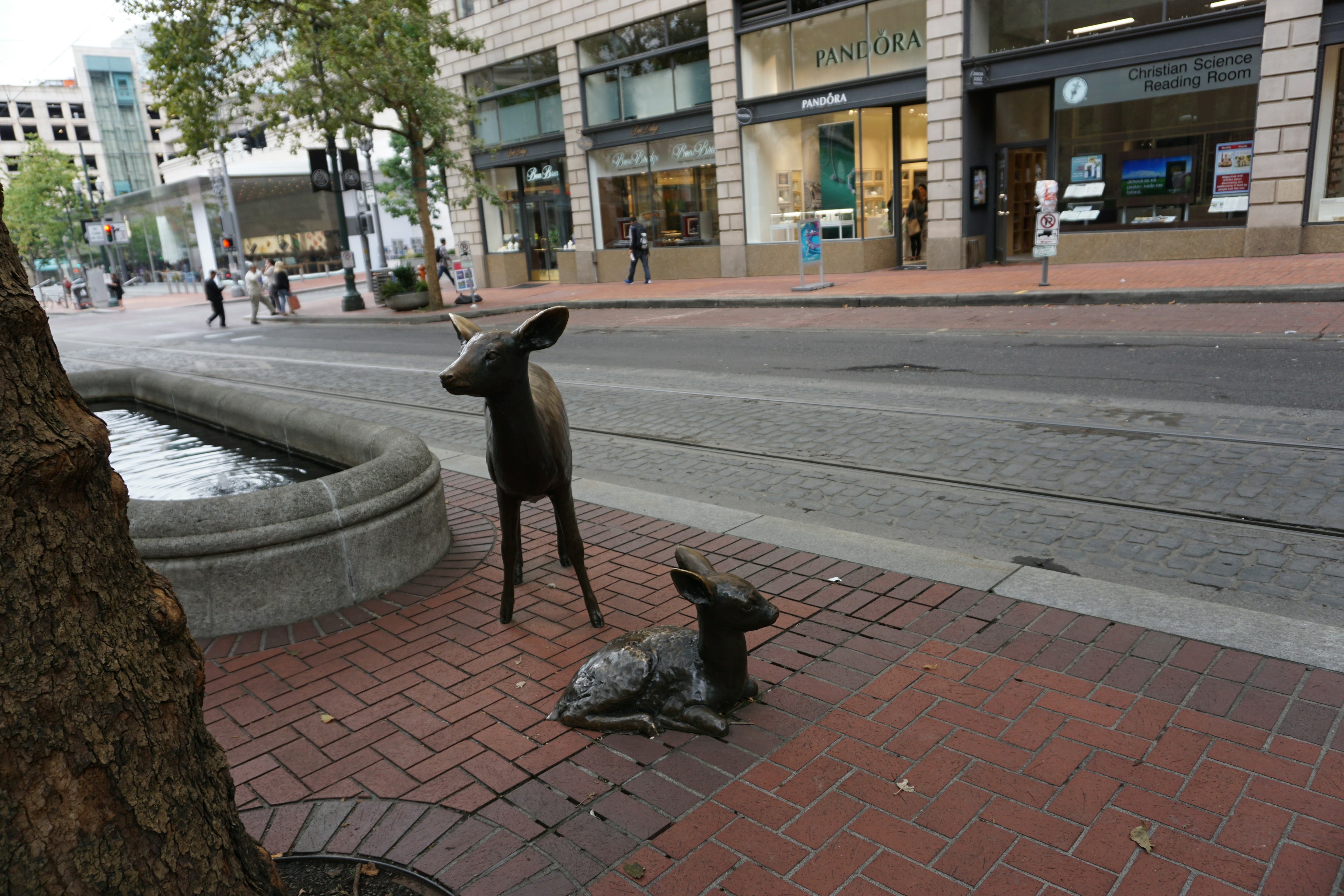 Sculptures of a deer and its fawn in an urban setting with people walking nearby