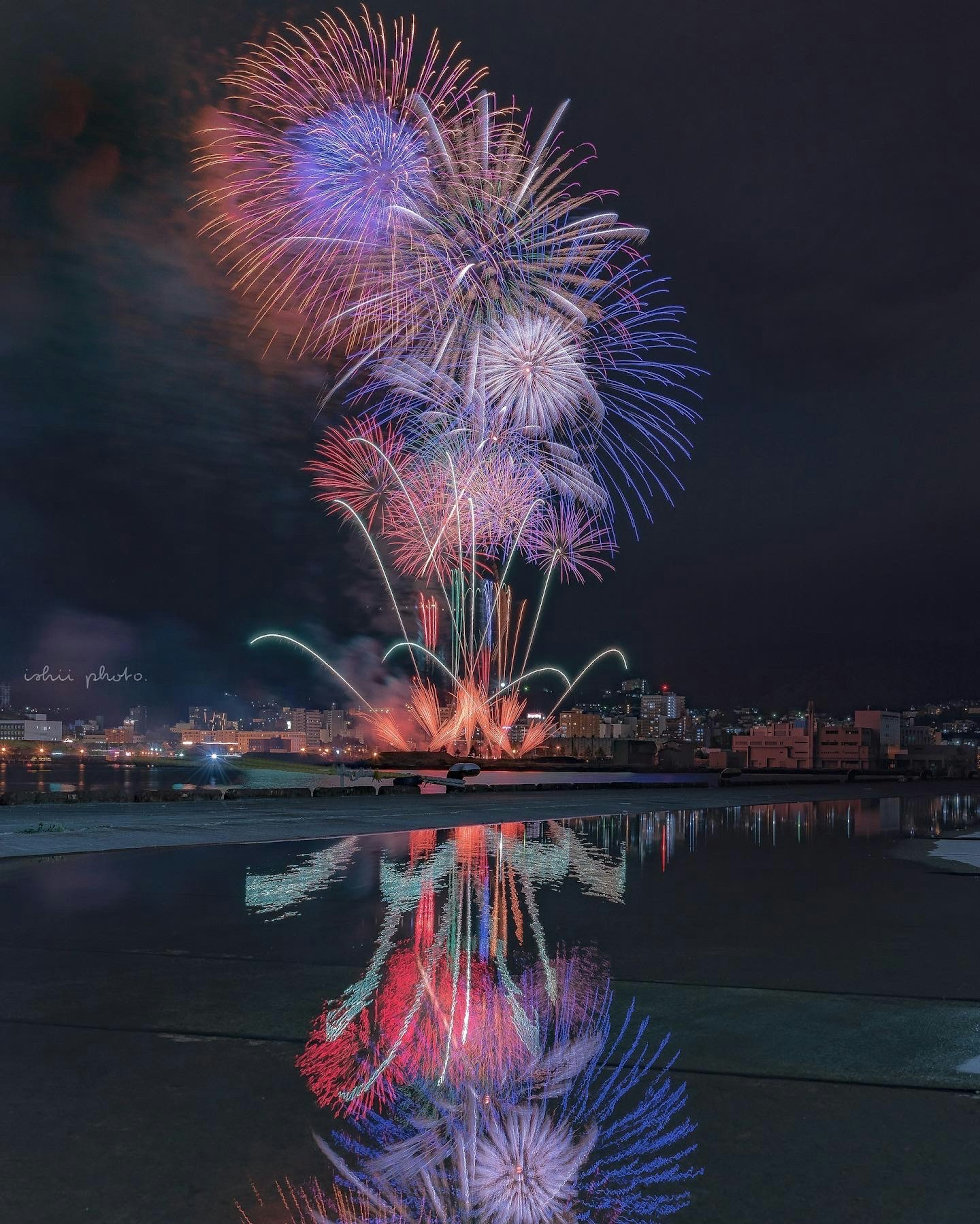 夜空に映える多彩な花火が水面に反射している美しい景色