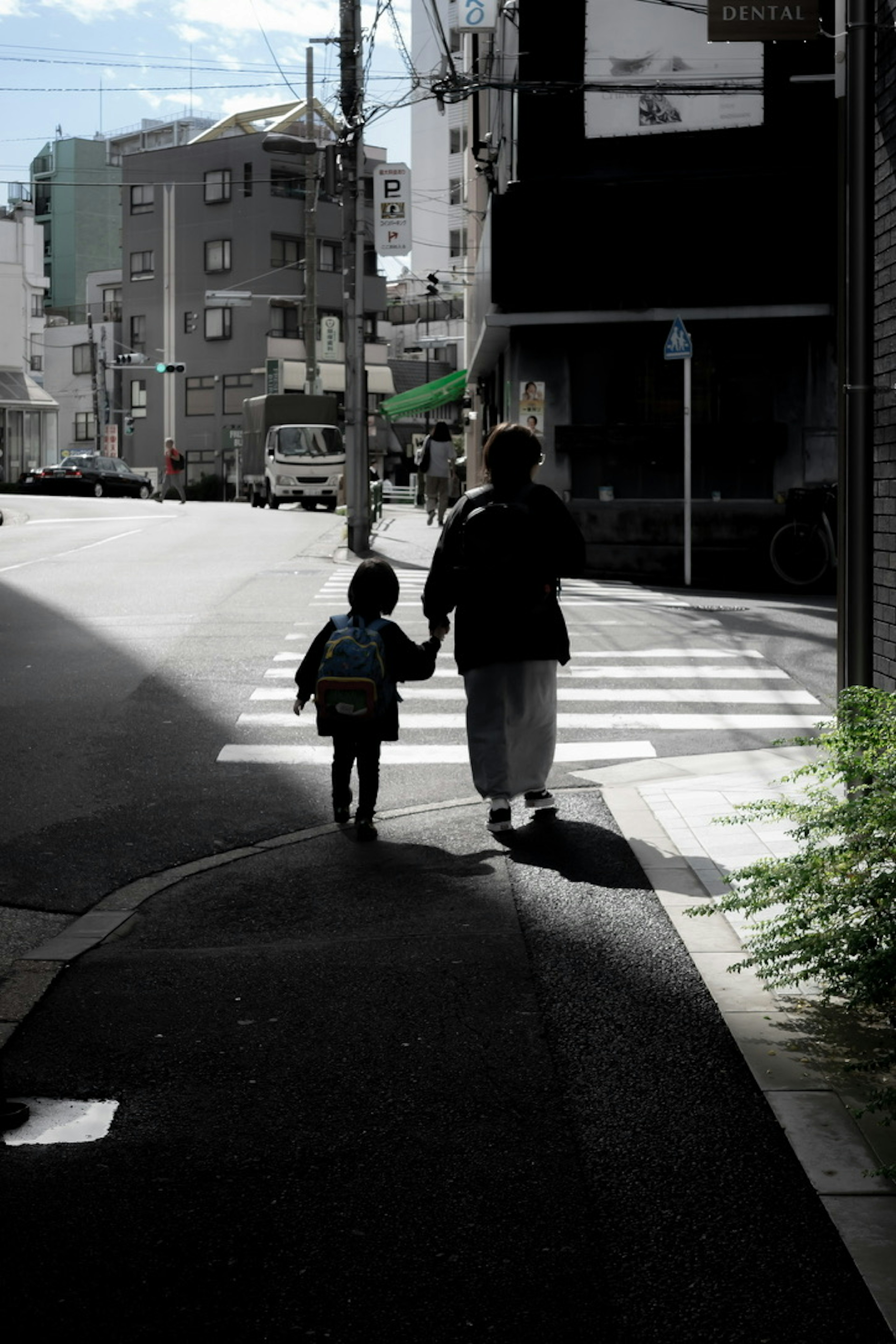 Silhouette eines Erwachsenen, der ein Kind an der Hand hält und eine Stadtstraße entlanggeht