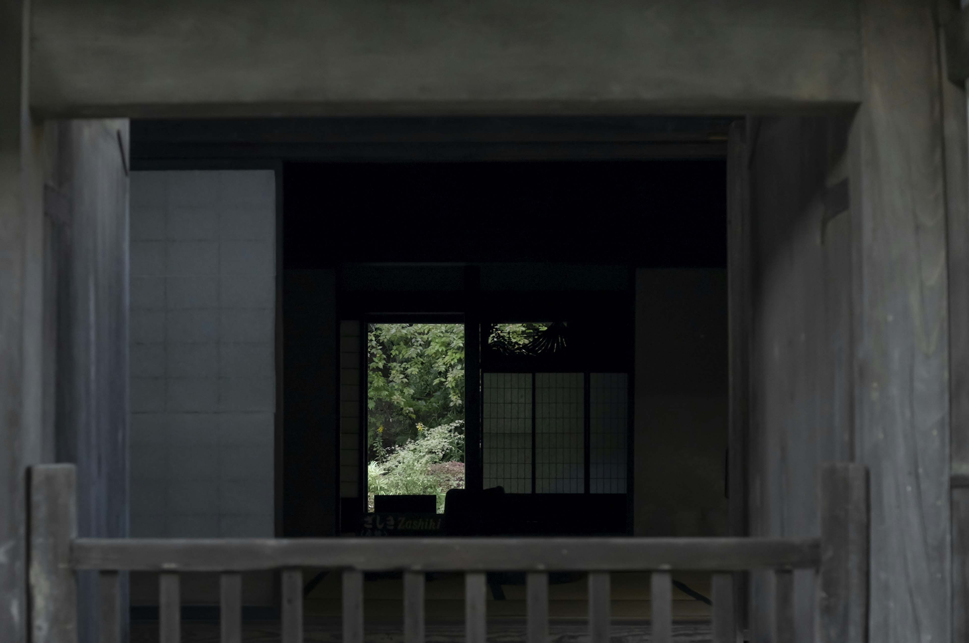 View of a garden through a dark entrance of a traditional Japanese house