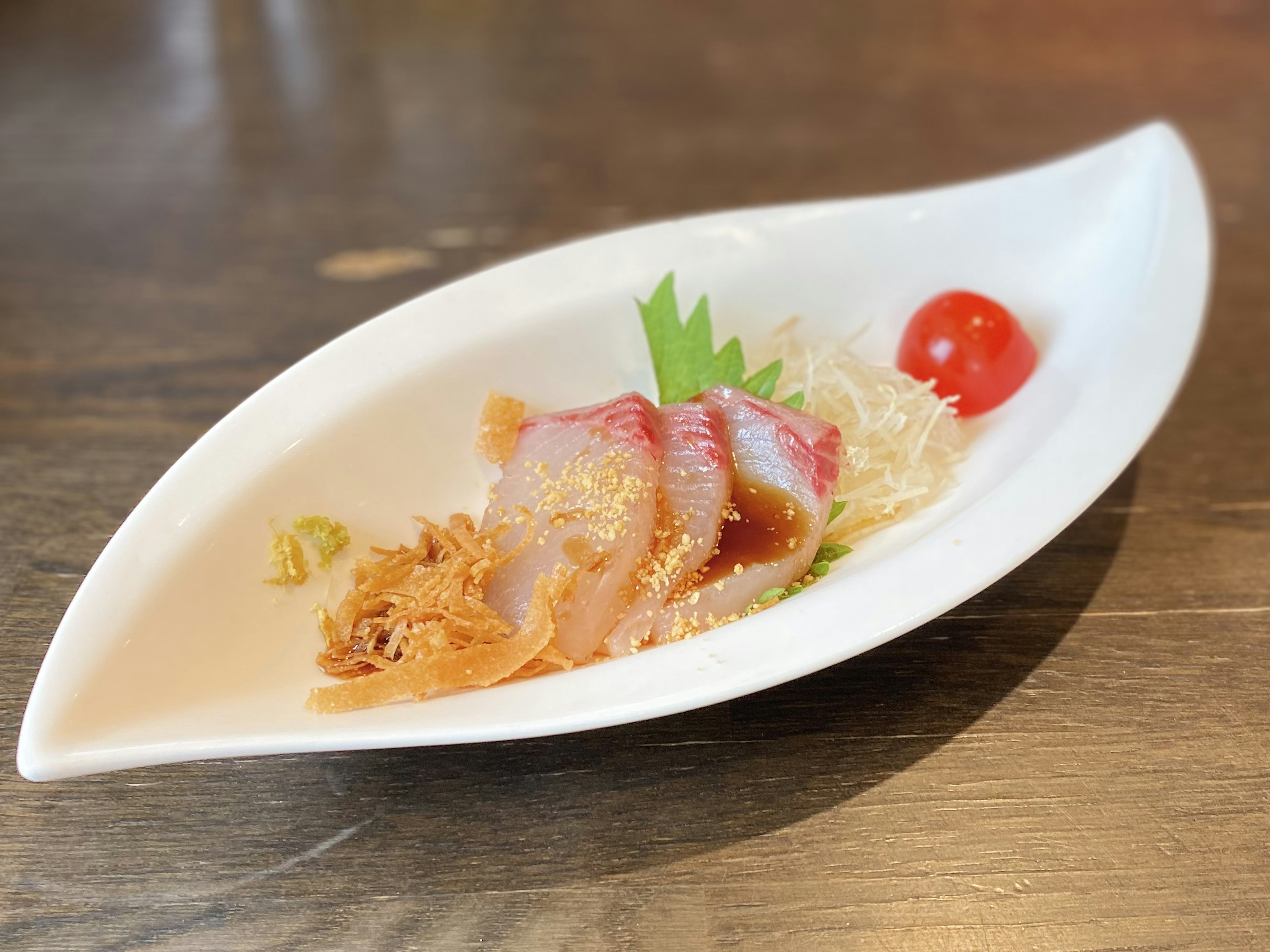 Sashimi servido en un plato blanco con un tomate cherry