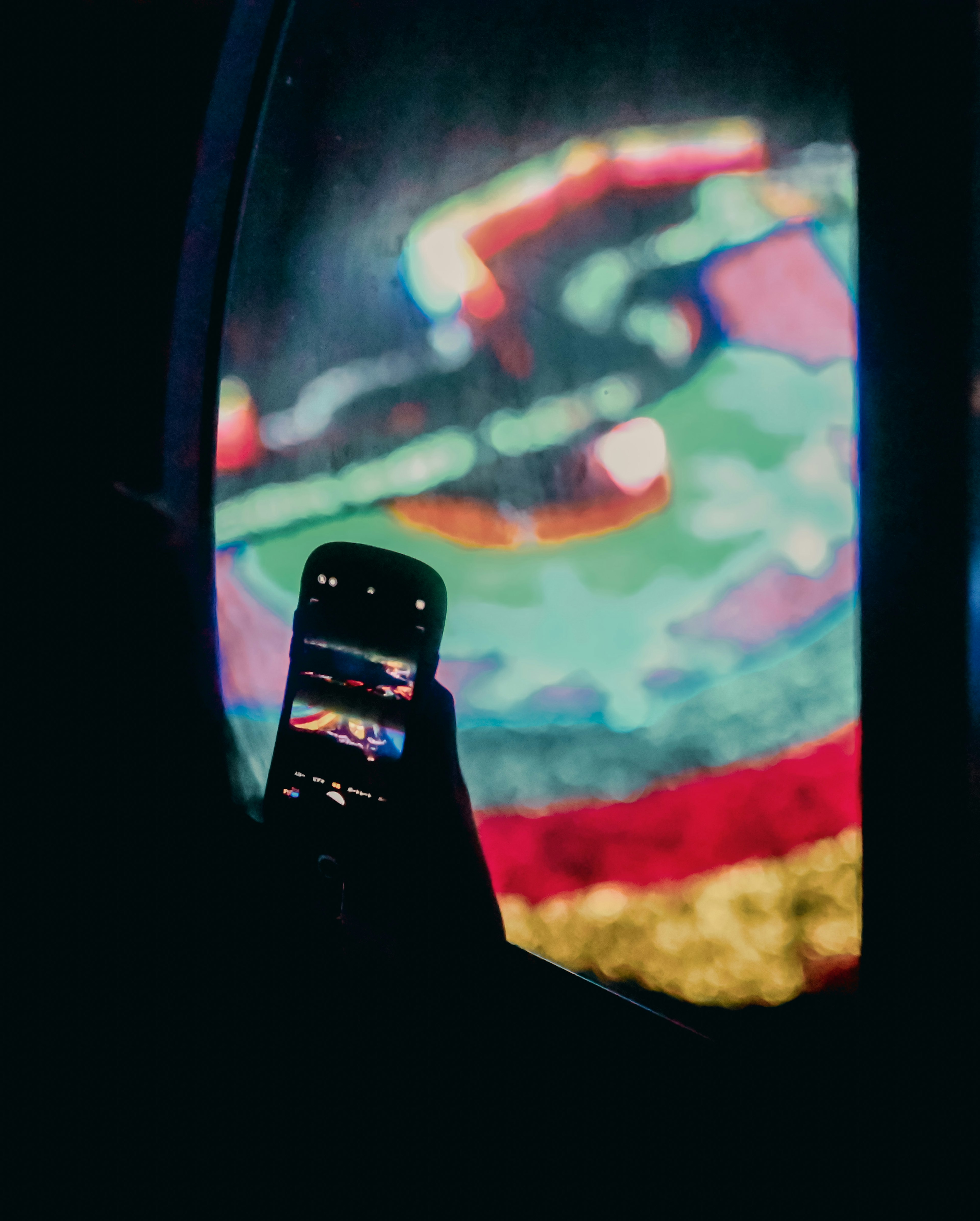 A hand holding a smartphone capturing vibrant visuals in a dark setting