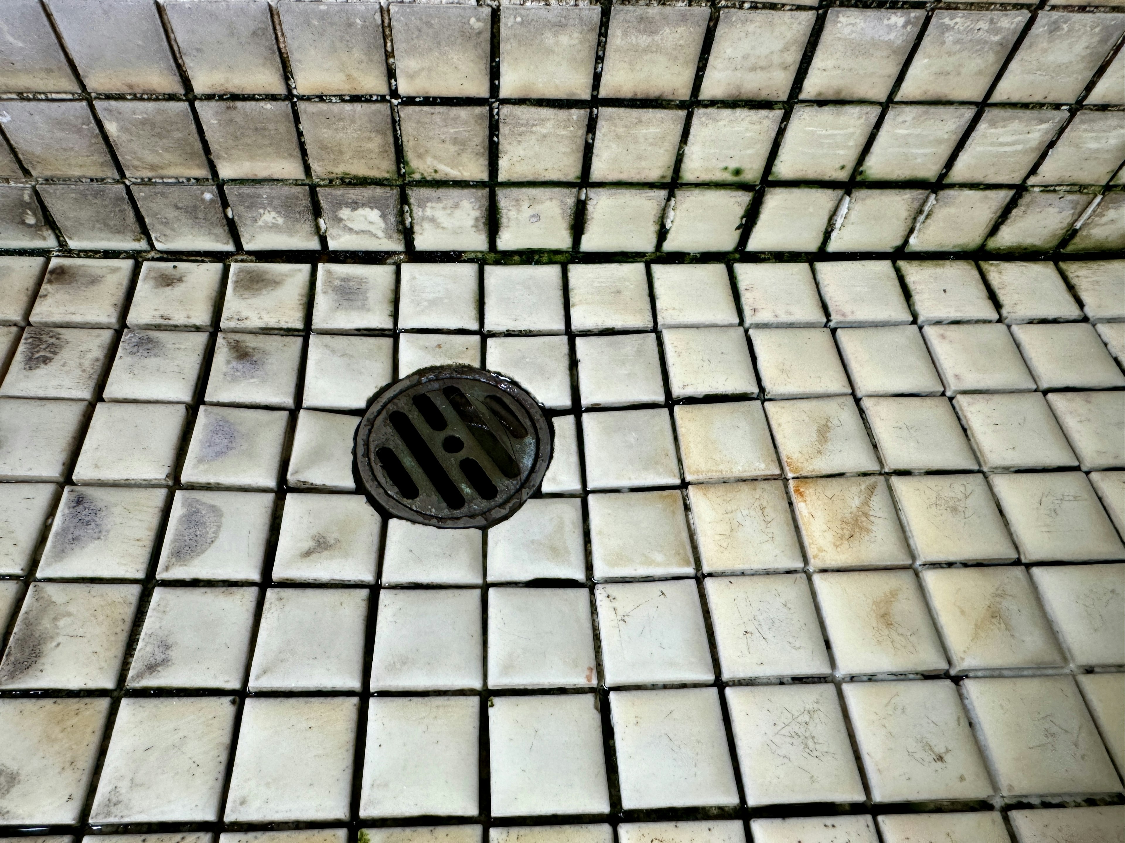 Image d'un sol de douche carrelé avec un drain et des carreaux anciens visibles