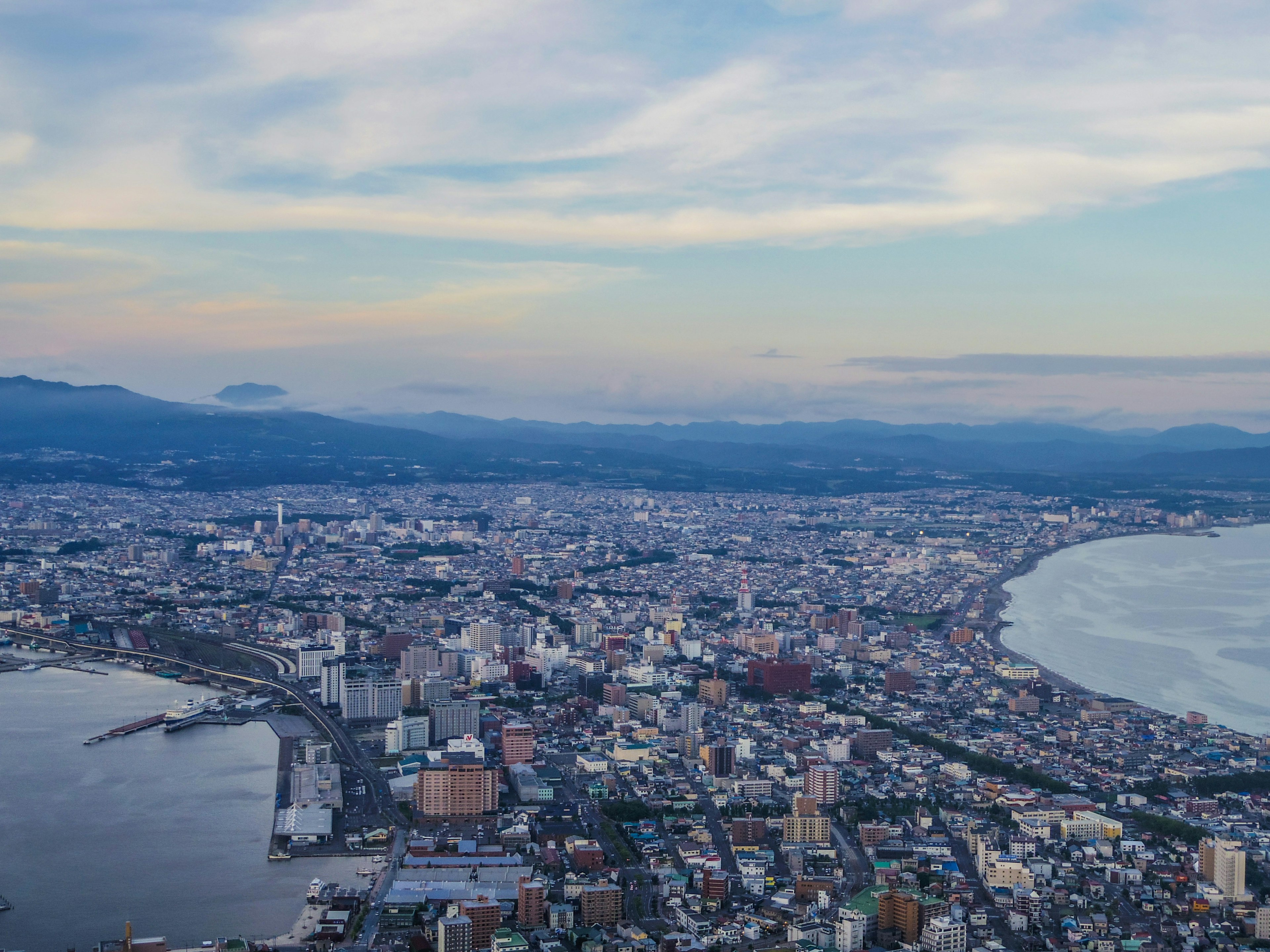 函馆市的航拍视图，展示了海岸线和城市景观，蓝天之下