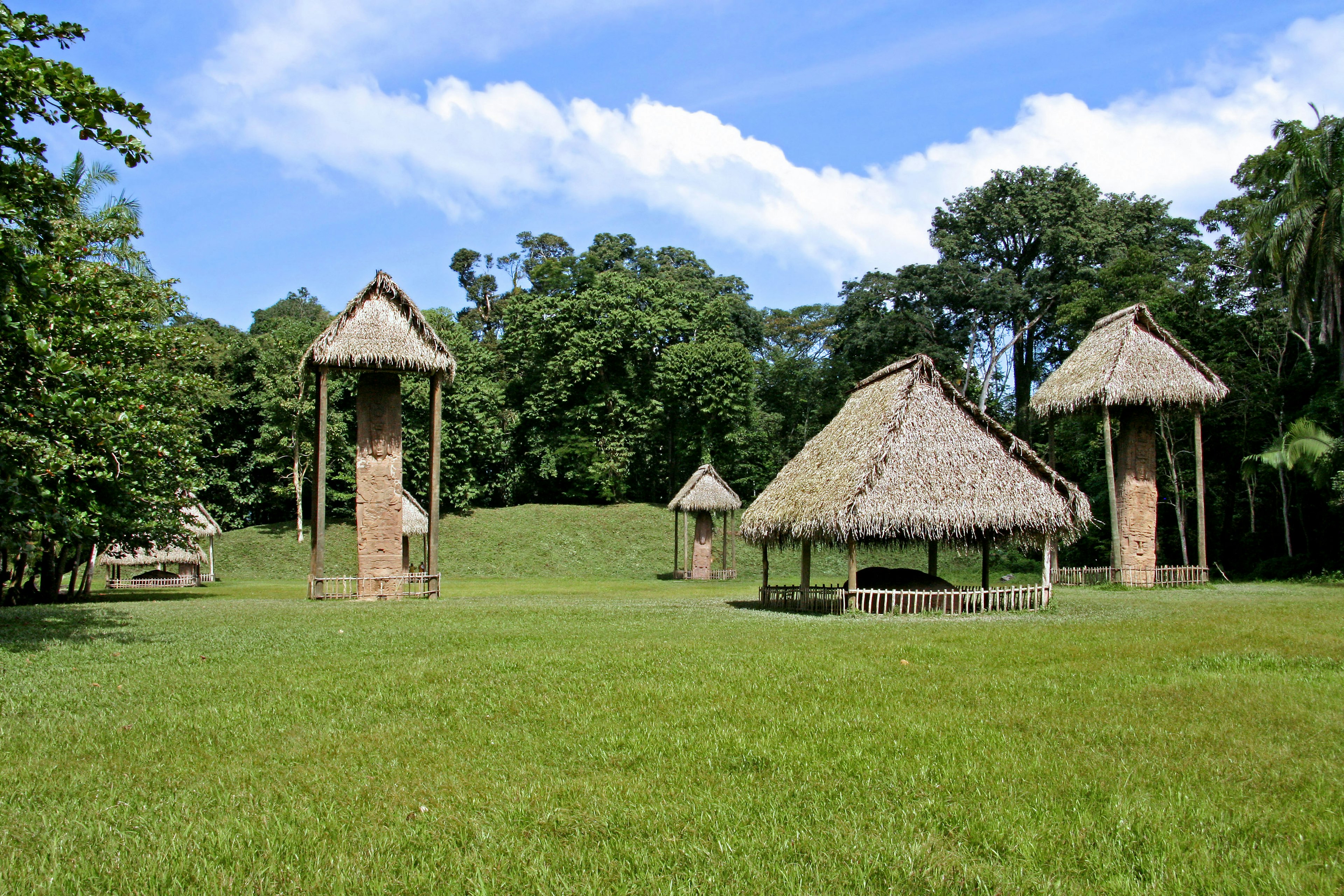 Traditionelle Strohhütten und Türme auf einer grünen Wiese unter blauem Himmel