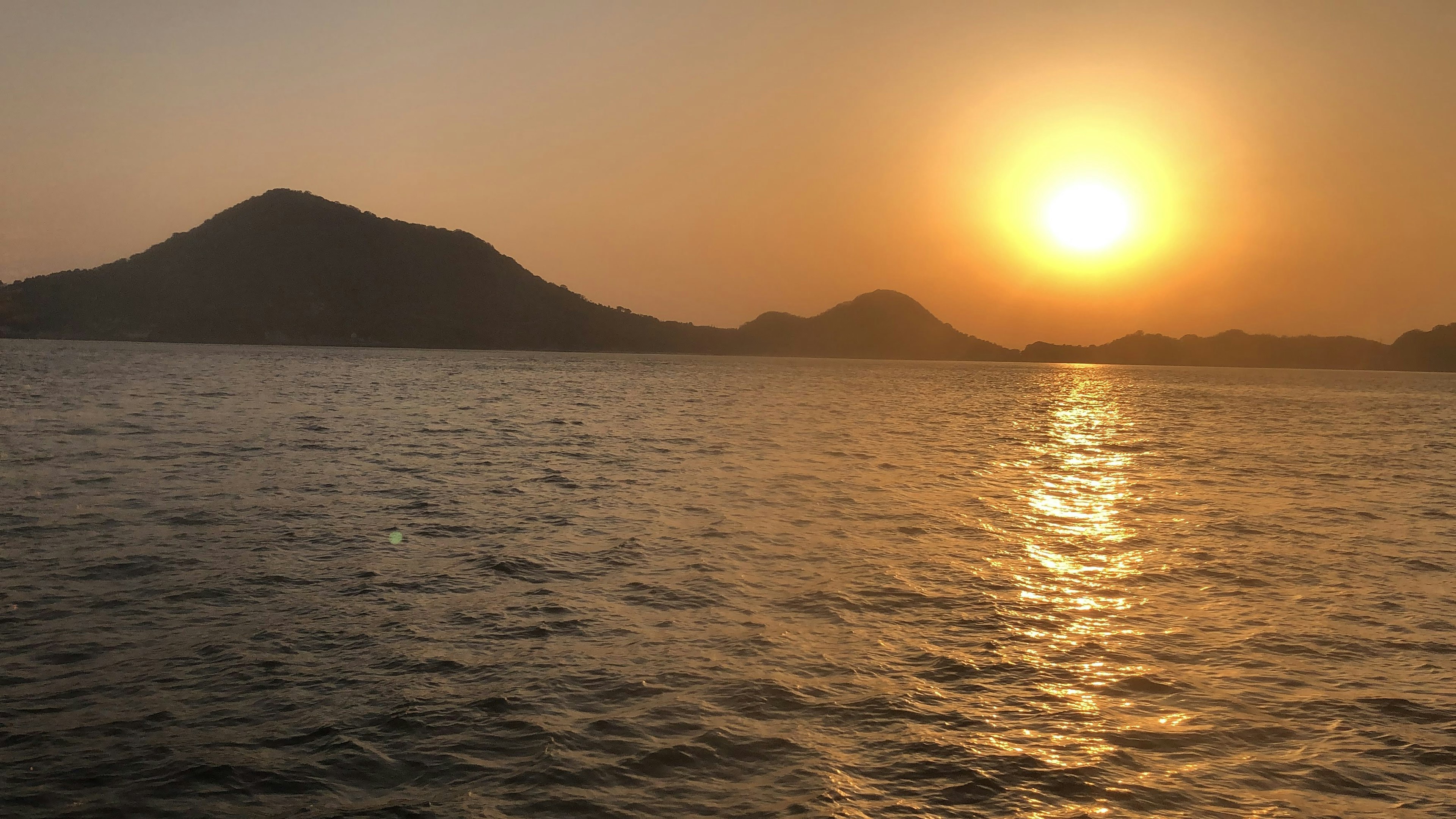 夕日が海に沈む風景 山と水面に反射する光