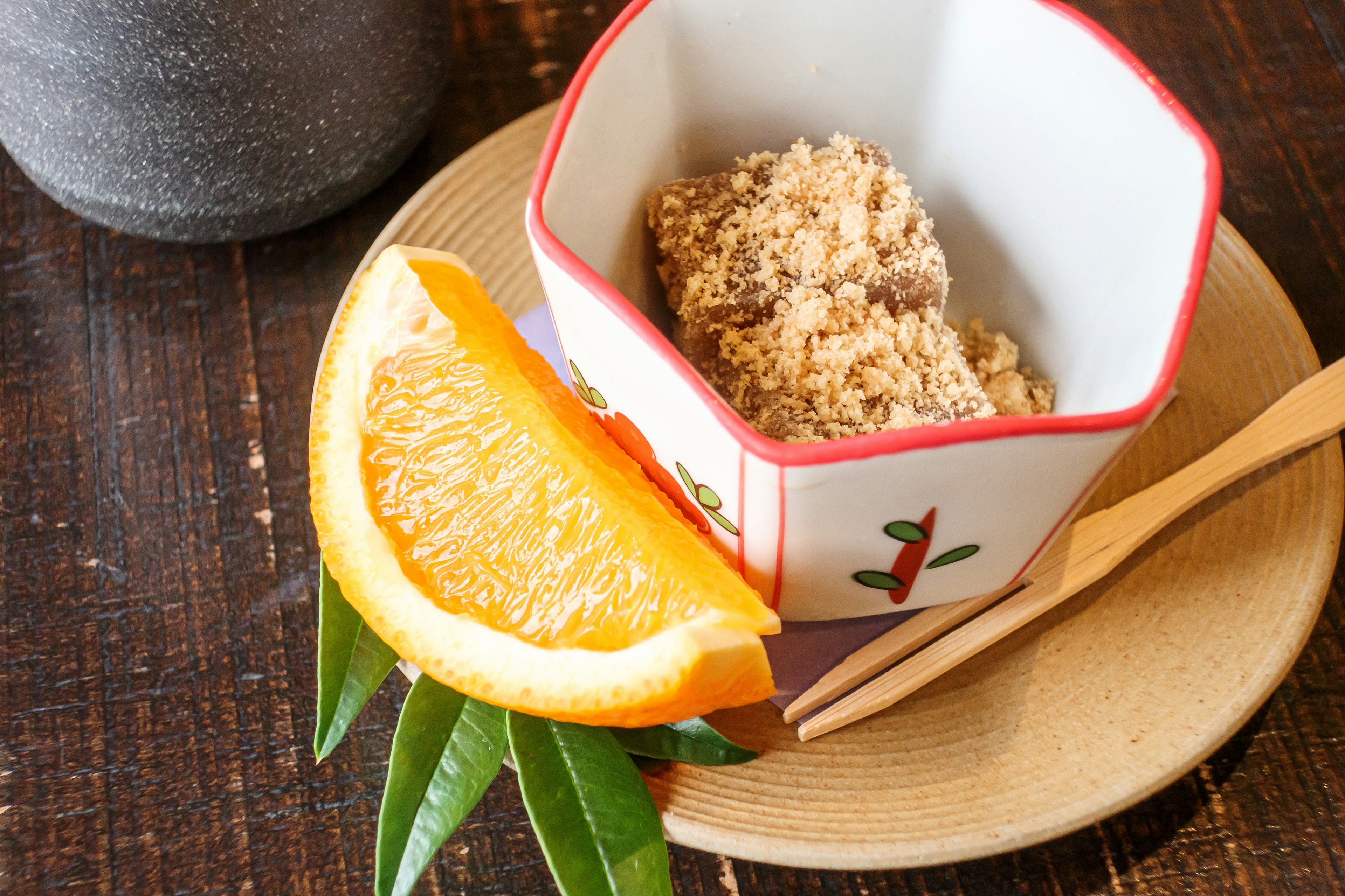 Plat de style japonais avec un bol contenant un aliment à côté d'une tranche d'orange et de feuilles