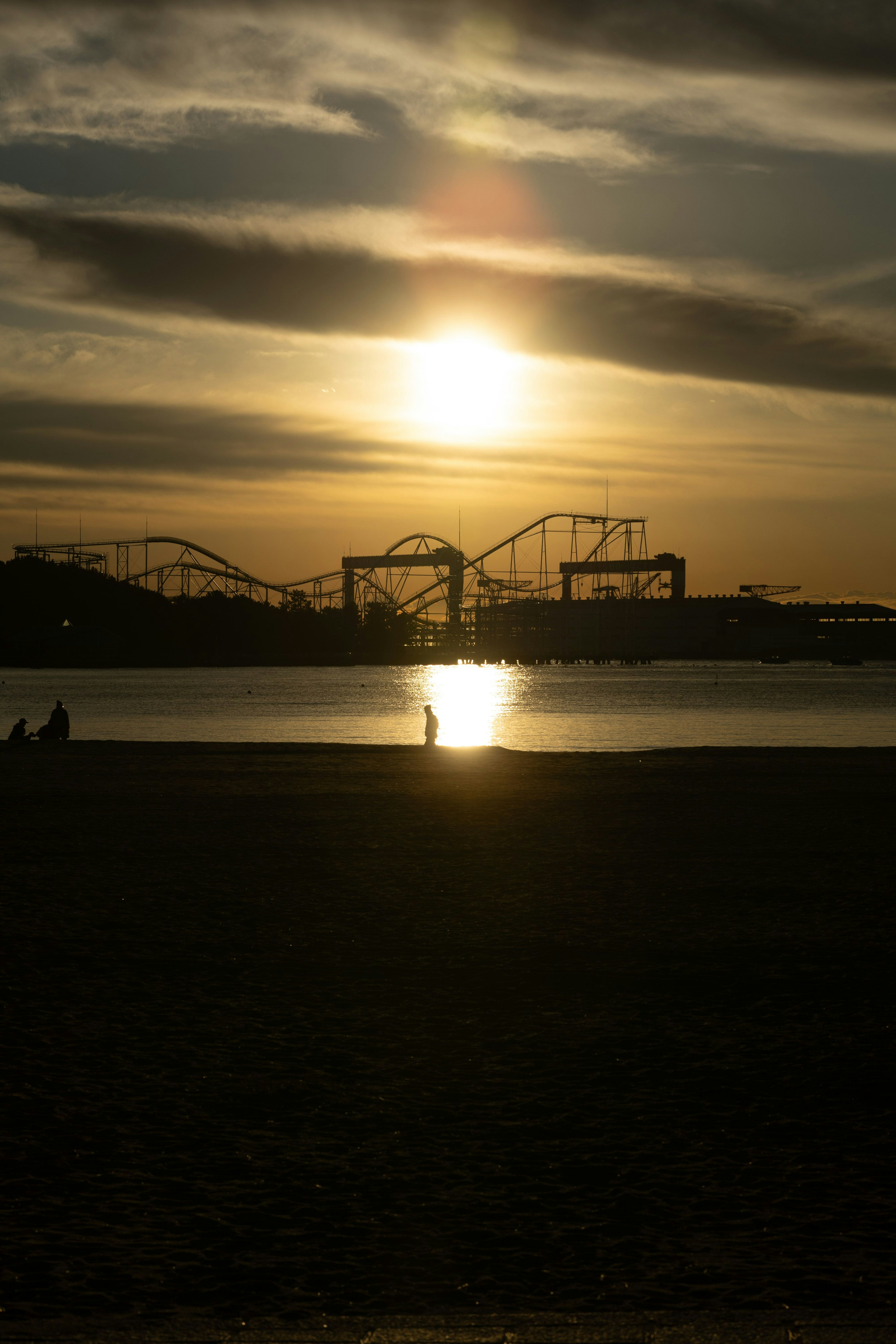 Scène côtière avec le coucher de soleil se reflétant sur l'eau montagnes russes de parc d'attractions au loin