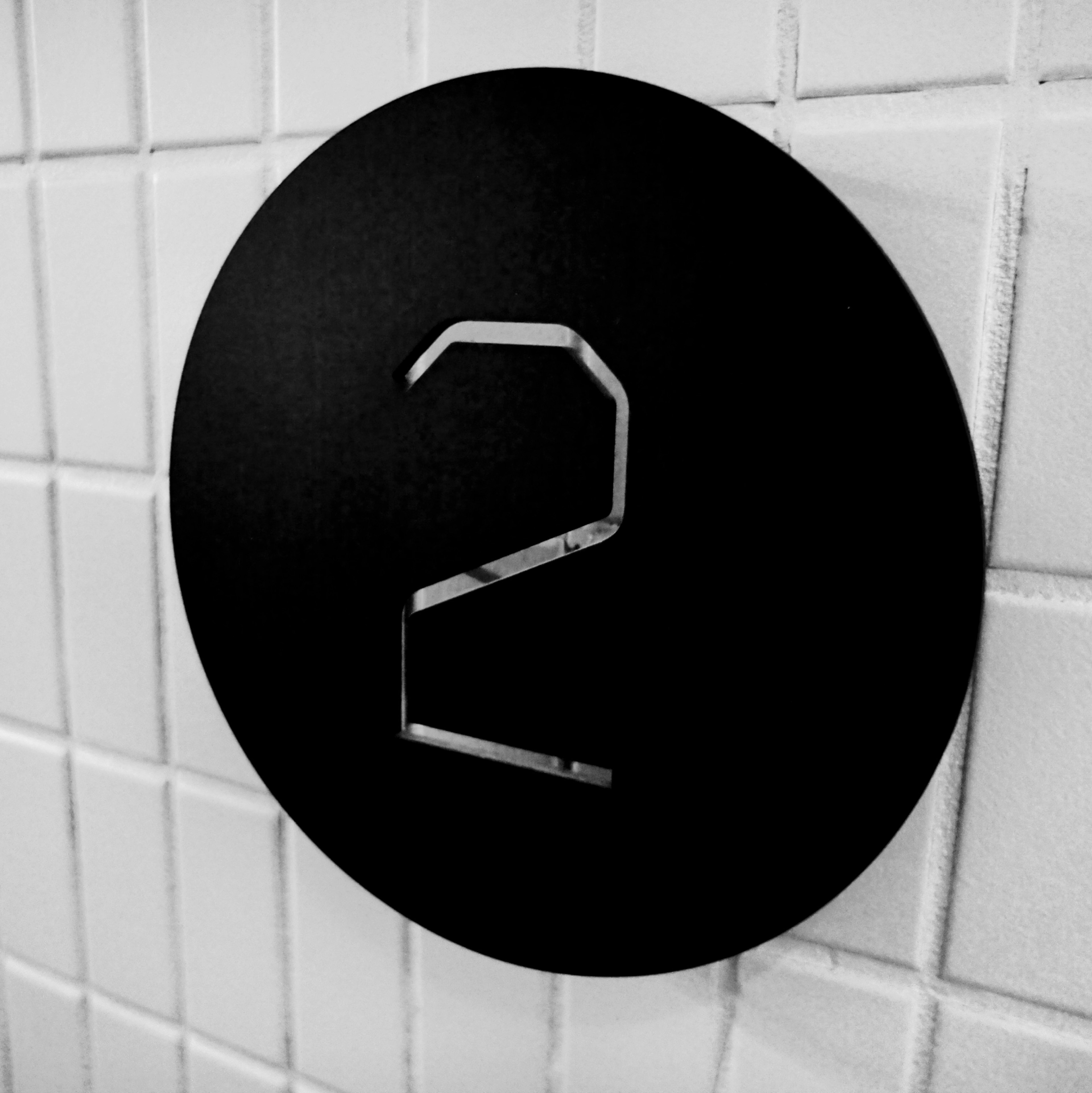 Black circular sign with a stainless steel number 2 embossed