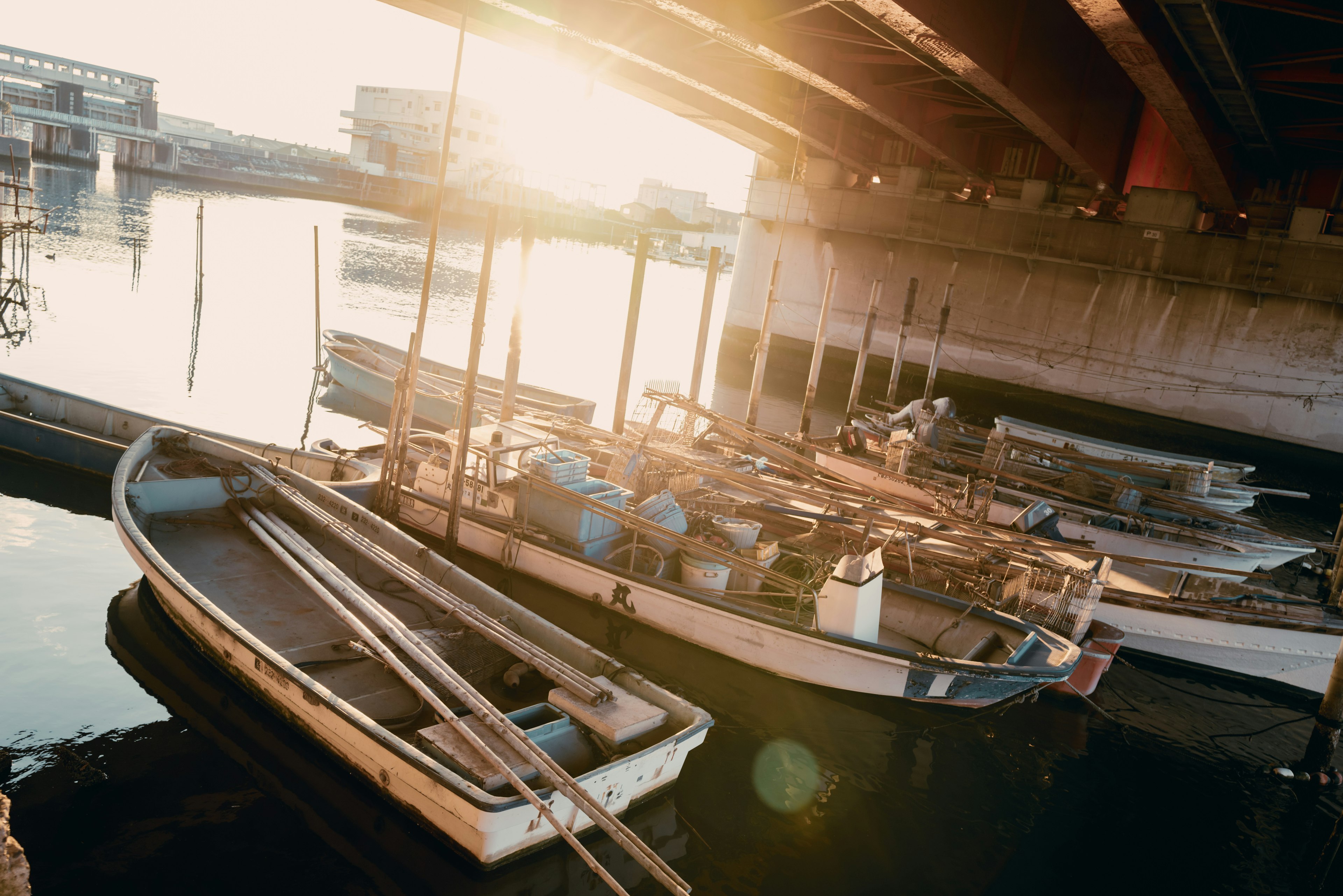 Barche e attrezzature da pesca sotto un ponte con luce solare riflessa sull'acqua