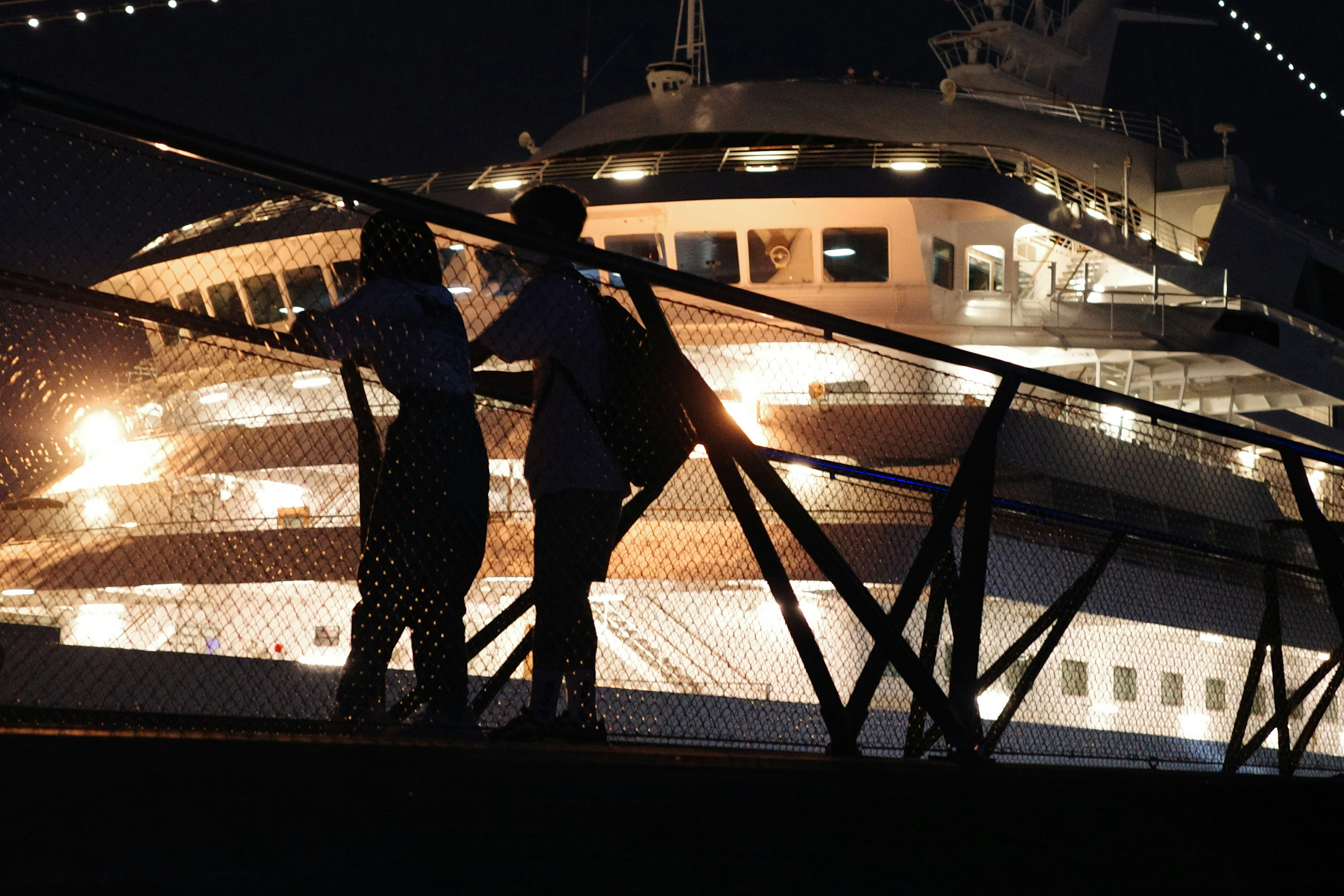 夜の港に浮かぶ豪華なクルーズ船とそれを眺めるカップル