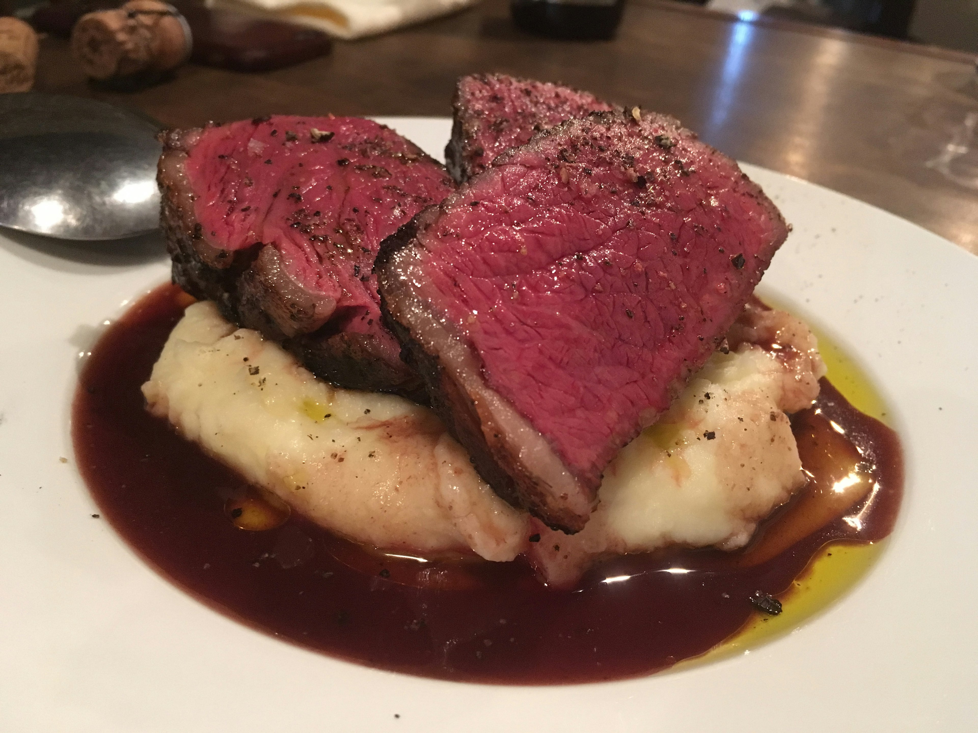 Rebanadas de carne jugosa sobre puré de patatas cremoso con un chorrito de salsa de vino tinto