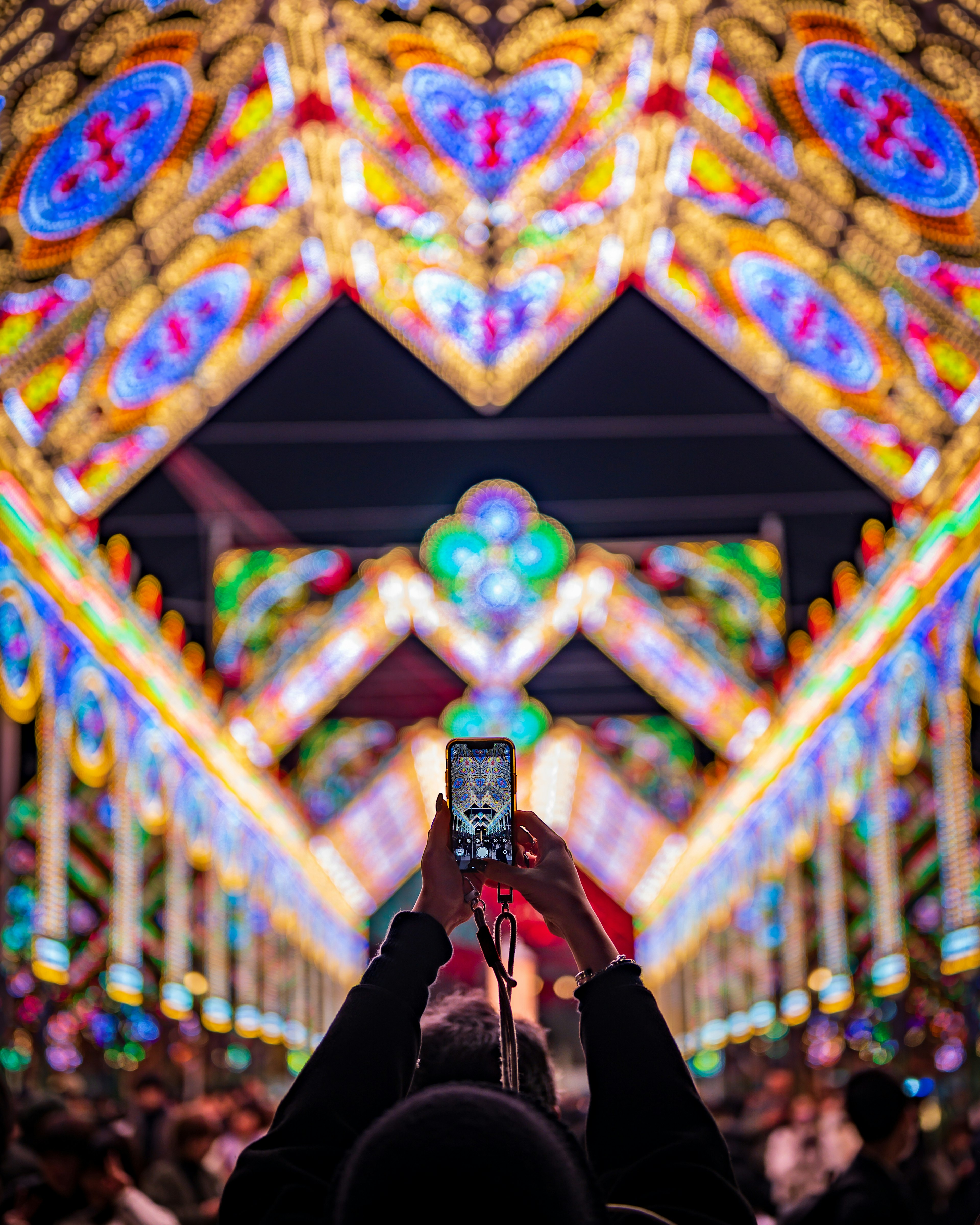 A person taking a photo with a smartphone under an arch decorated with colorful lights