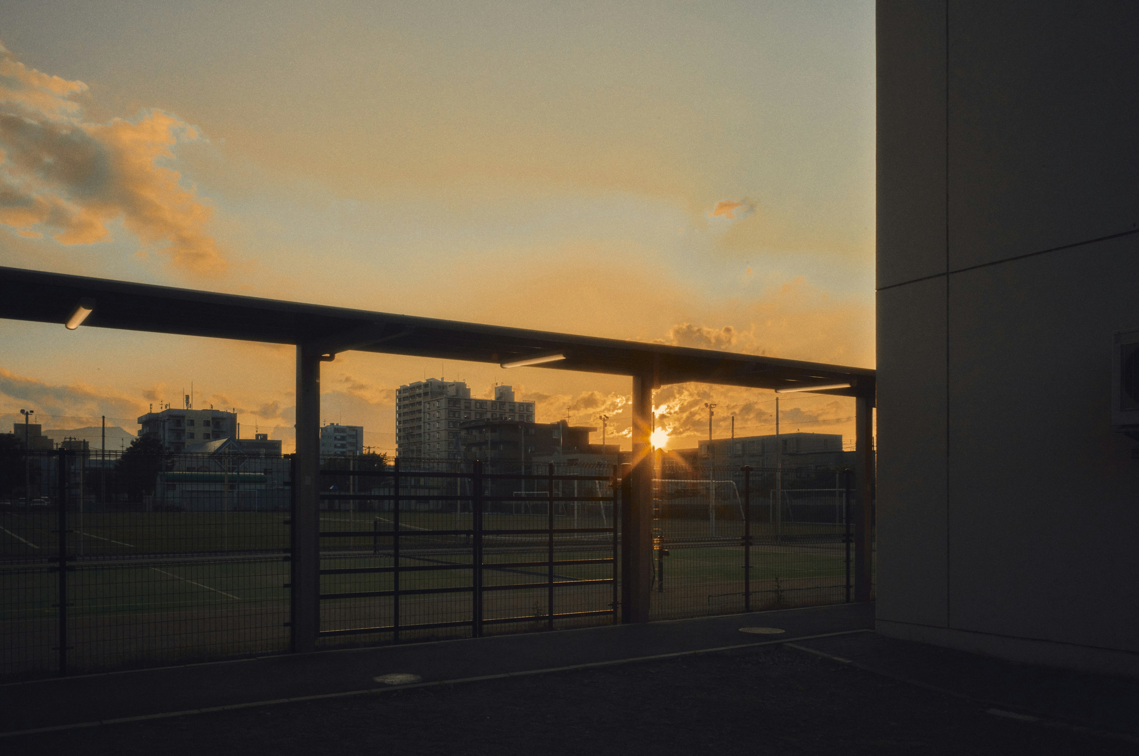 Sonnenuntergang zwischen Gebäuden mit einem Zaun