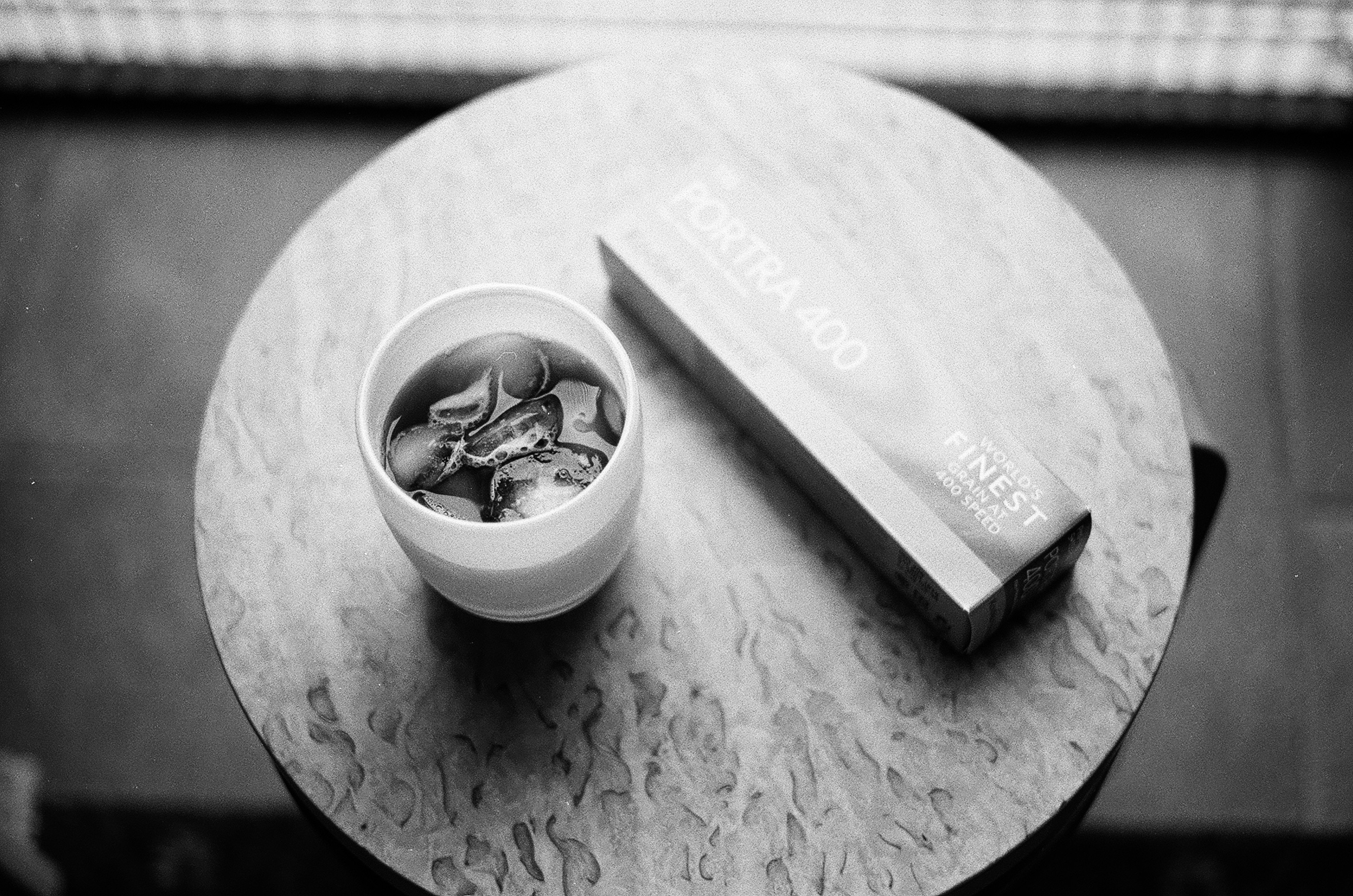 Black and white image featuring a white cup and a book on a round table