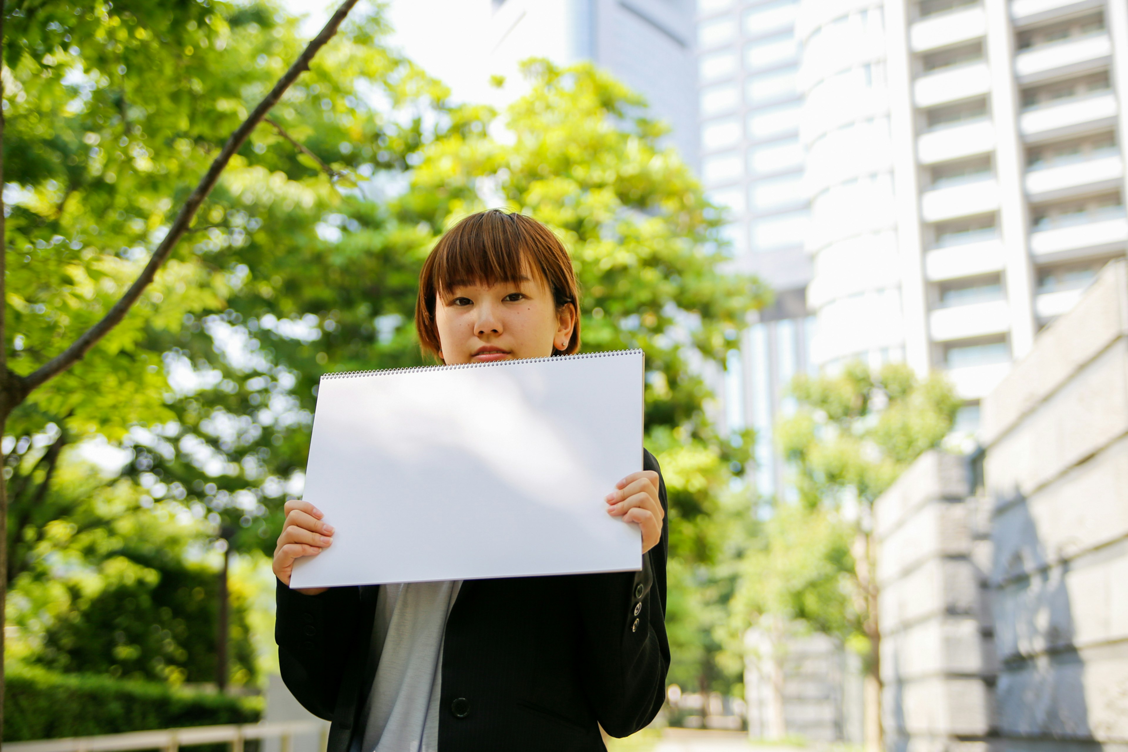 緑の木々と高層ビルの背景に白い紙を持つ女性