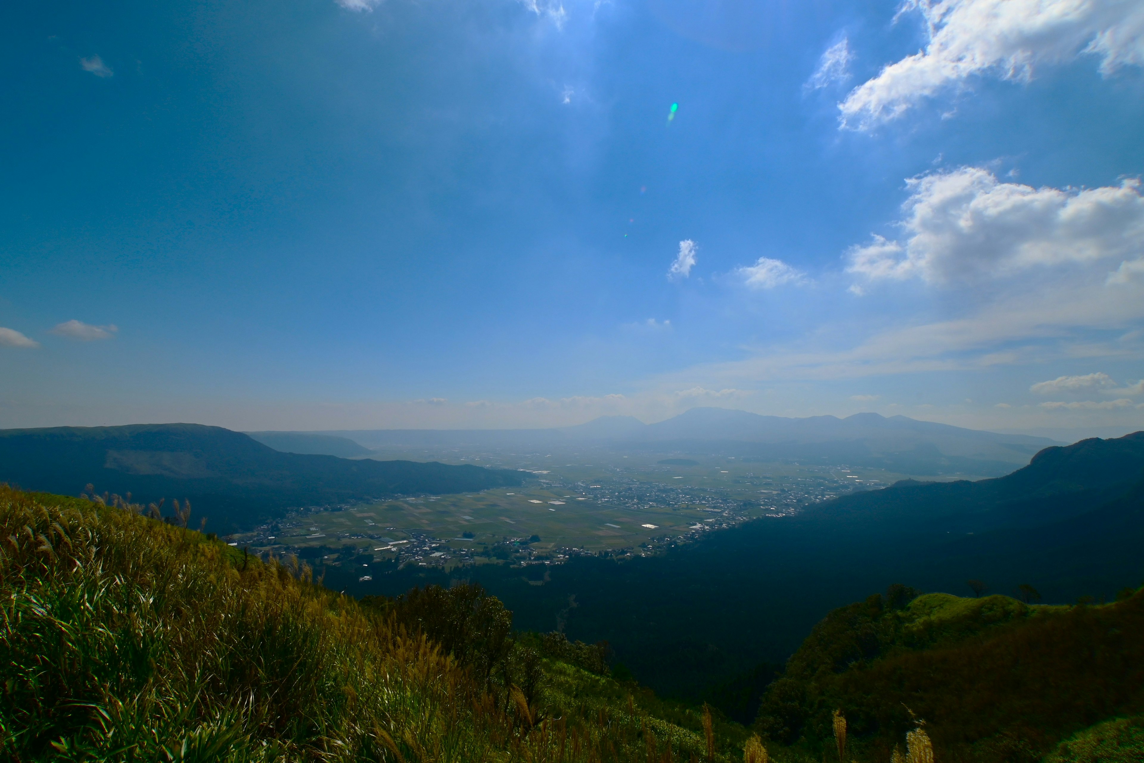 青い空と雲が広がる美しい風景の中に、山々と谷が見える