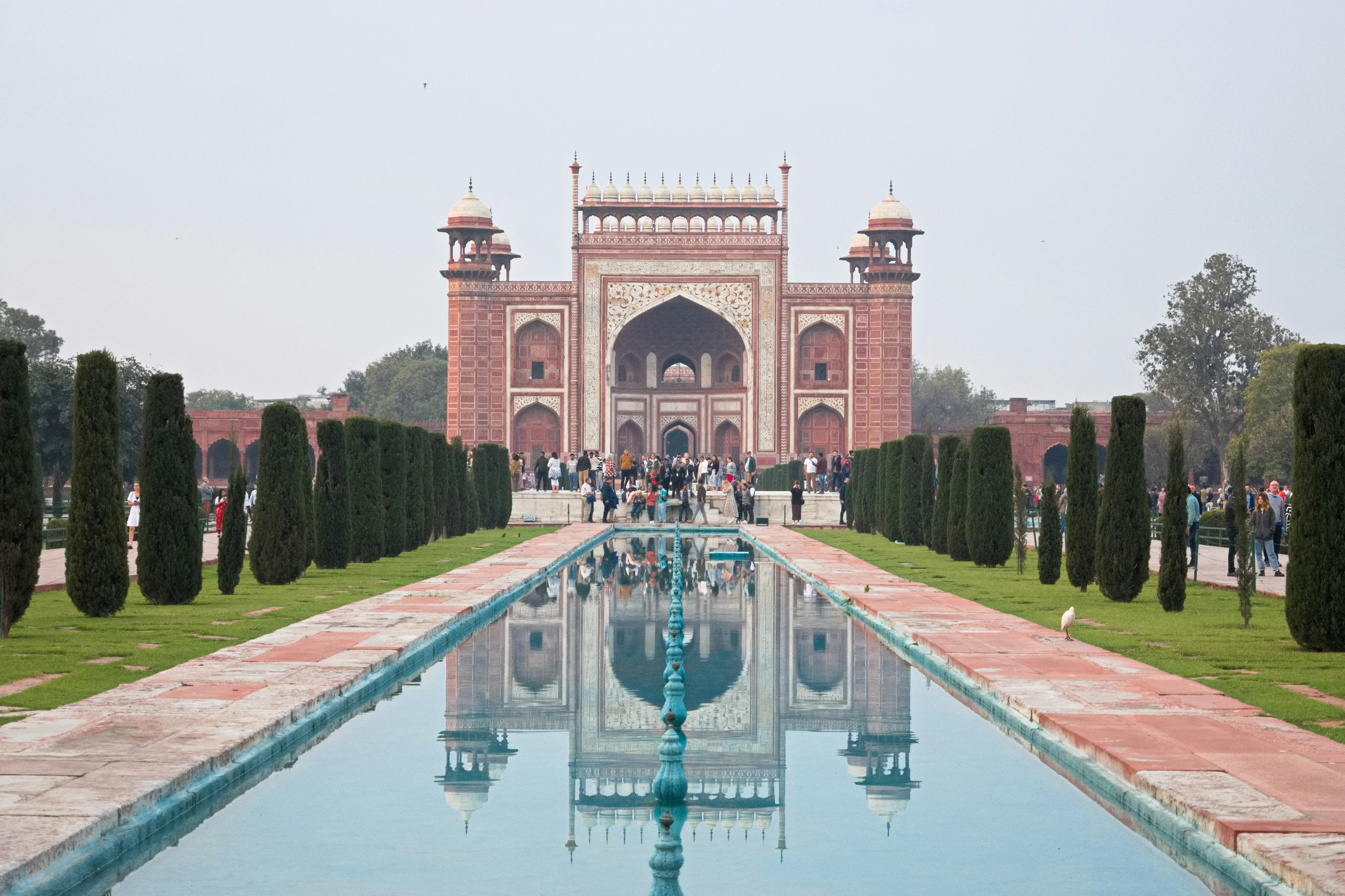 Pemandangan pintu masuk Taj Mahal dengan kolam refleksi dan vegetasi subur