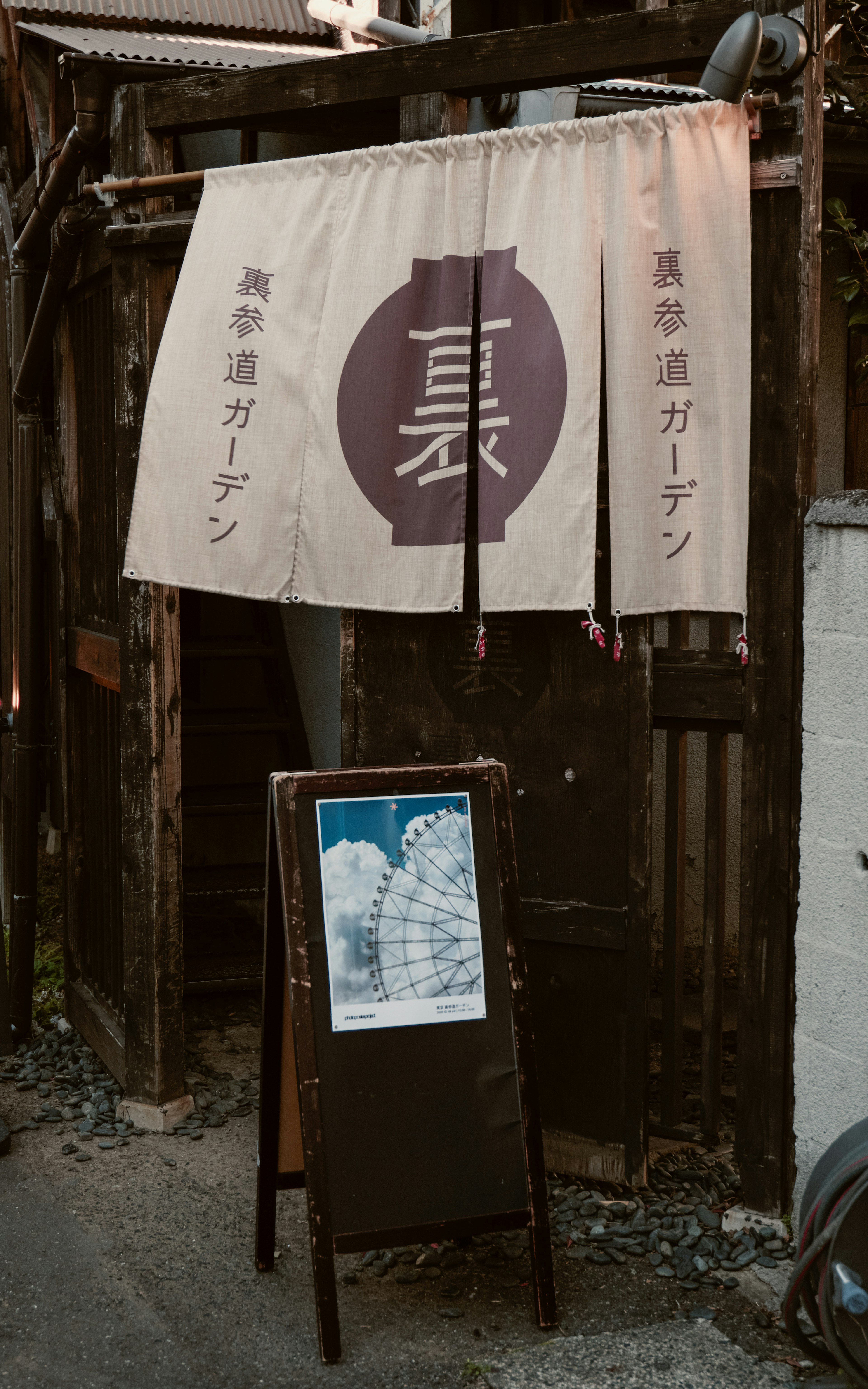 Entrada de un antiguo edificio de madera con un noren y un cartel de menú escrito a mano