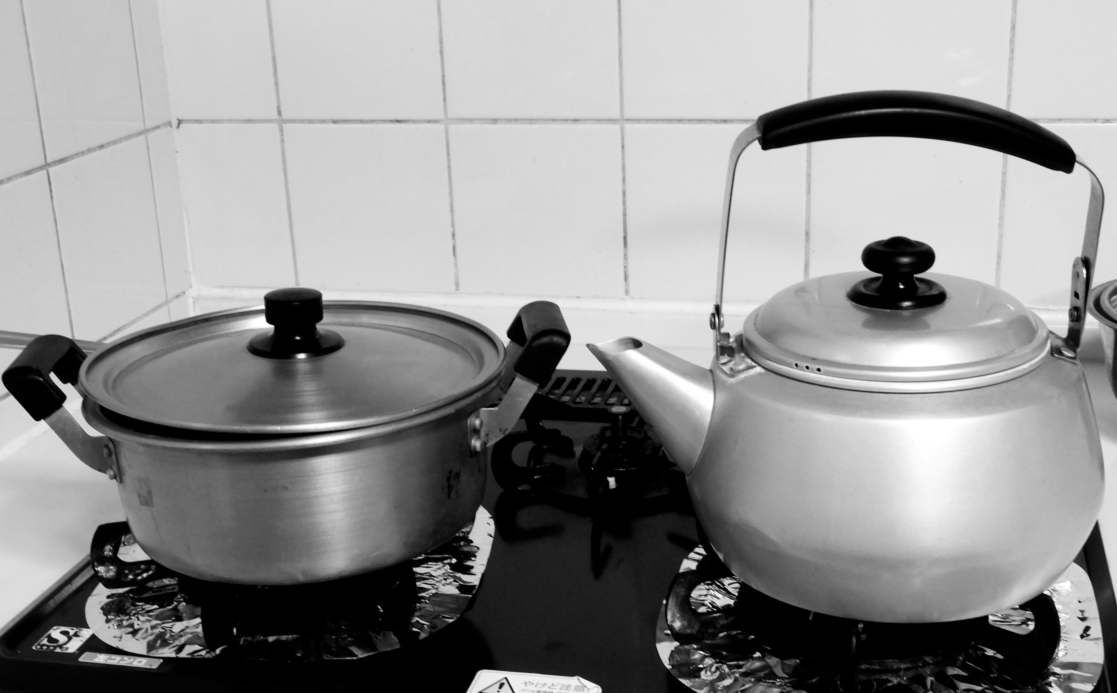 A pot and kettle placed side by side on a stove in black and white