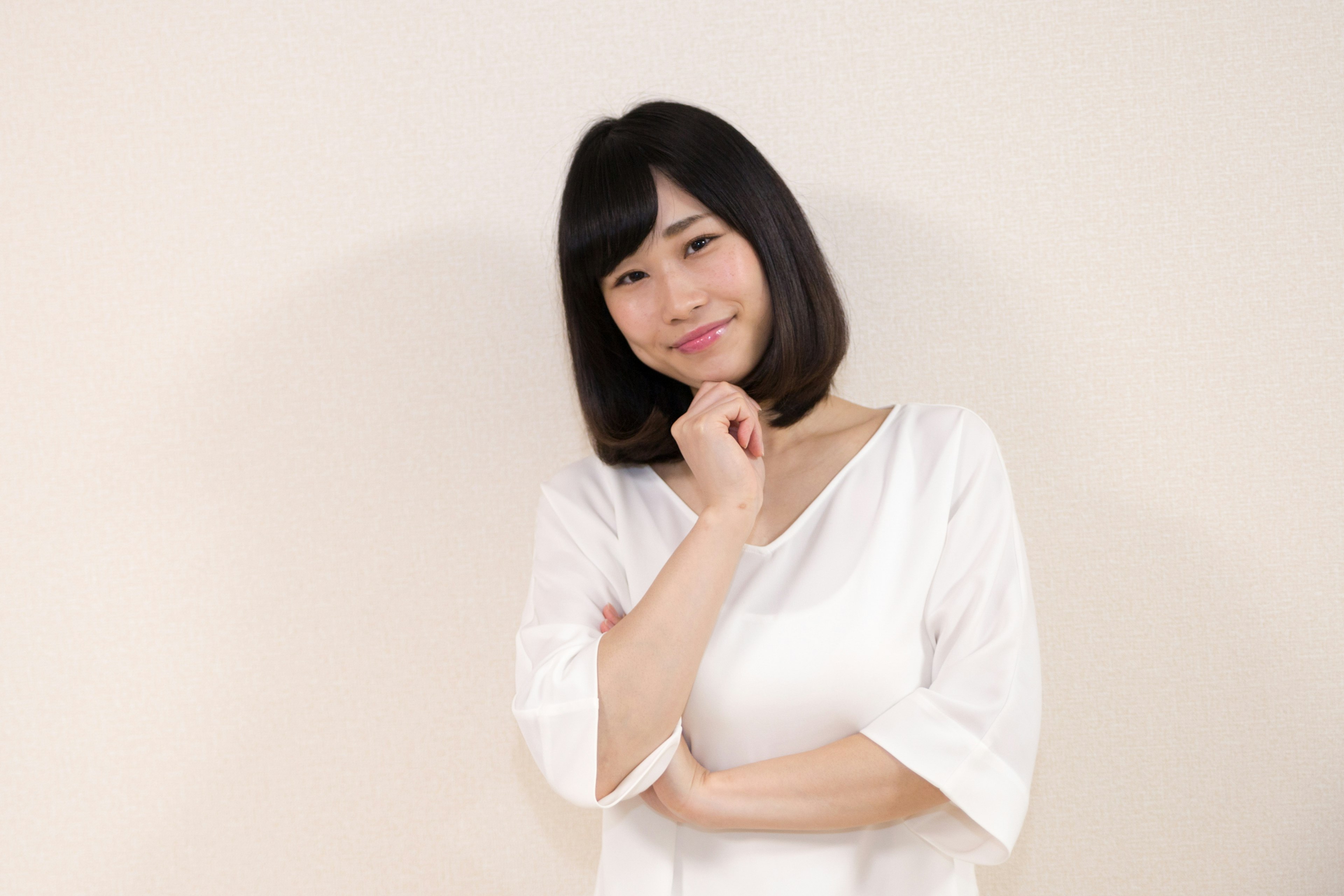 Woman in white top smiling thoughtfully with hand on chin