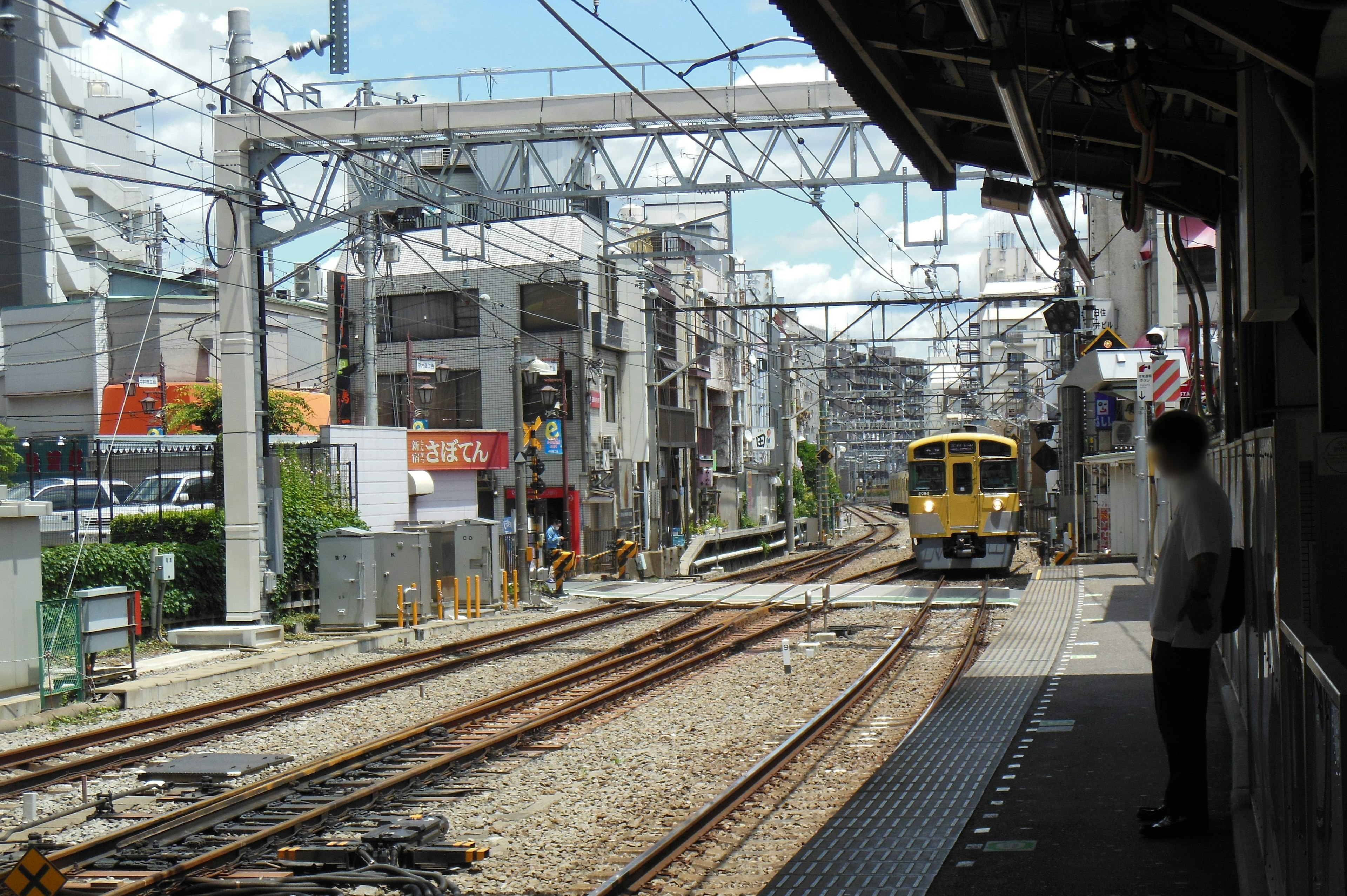 Un treno che si avvicina a una stazione con edifici commerciali e cielo blu sullo sfondo