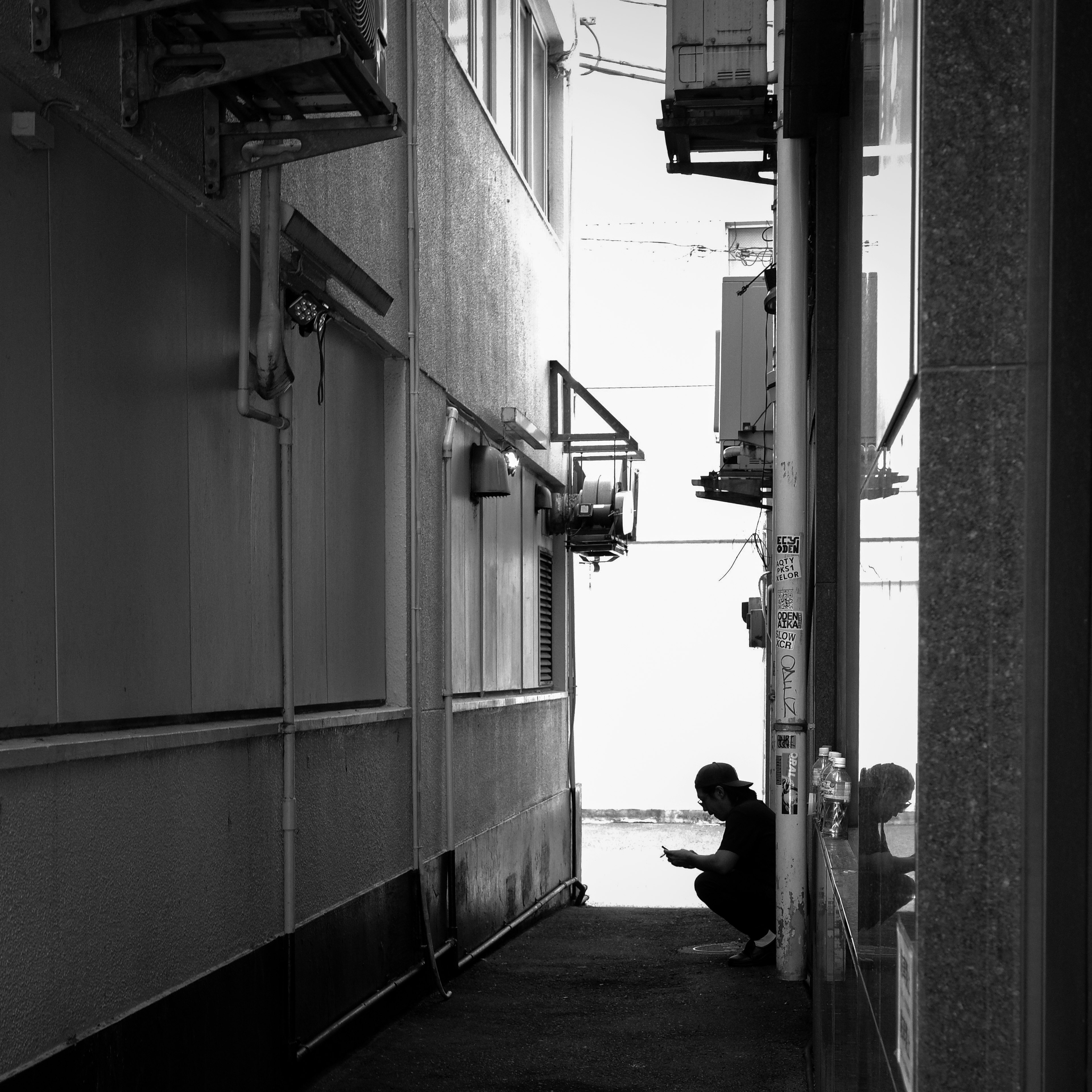 Silhouette of a person sitting in a narrow alleyway between buildings