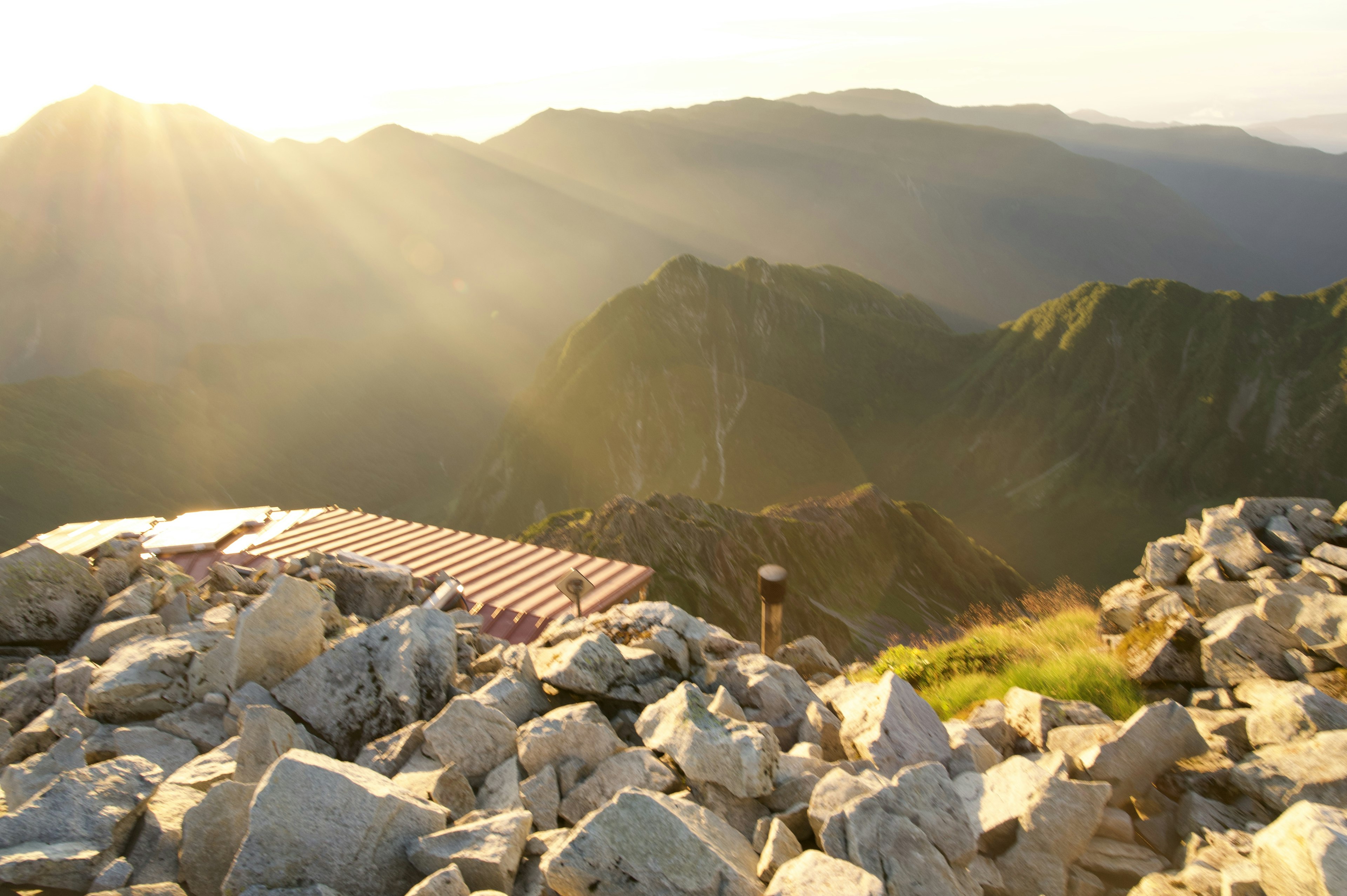 Landschaft mit Sonnenlicht, das über die Berge strömt, steiniger Vordergrund mit einem kleinen Unterstand