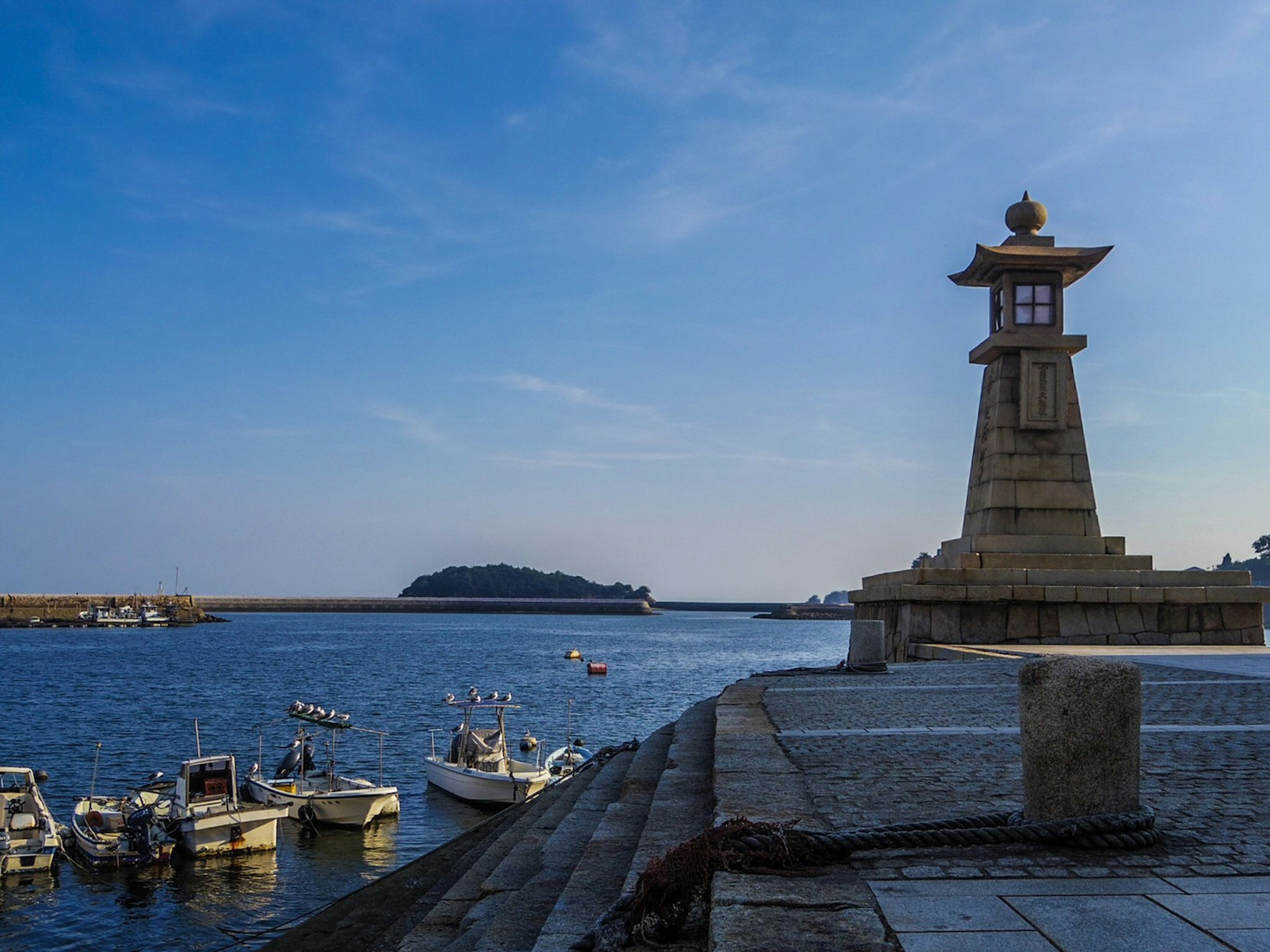 Vista escénica de un faro en el puerto con barcos de pesca y cielo azul claro