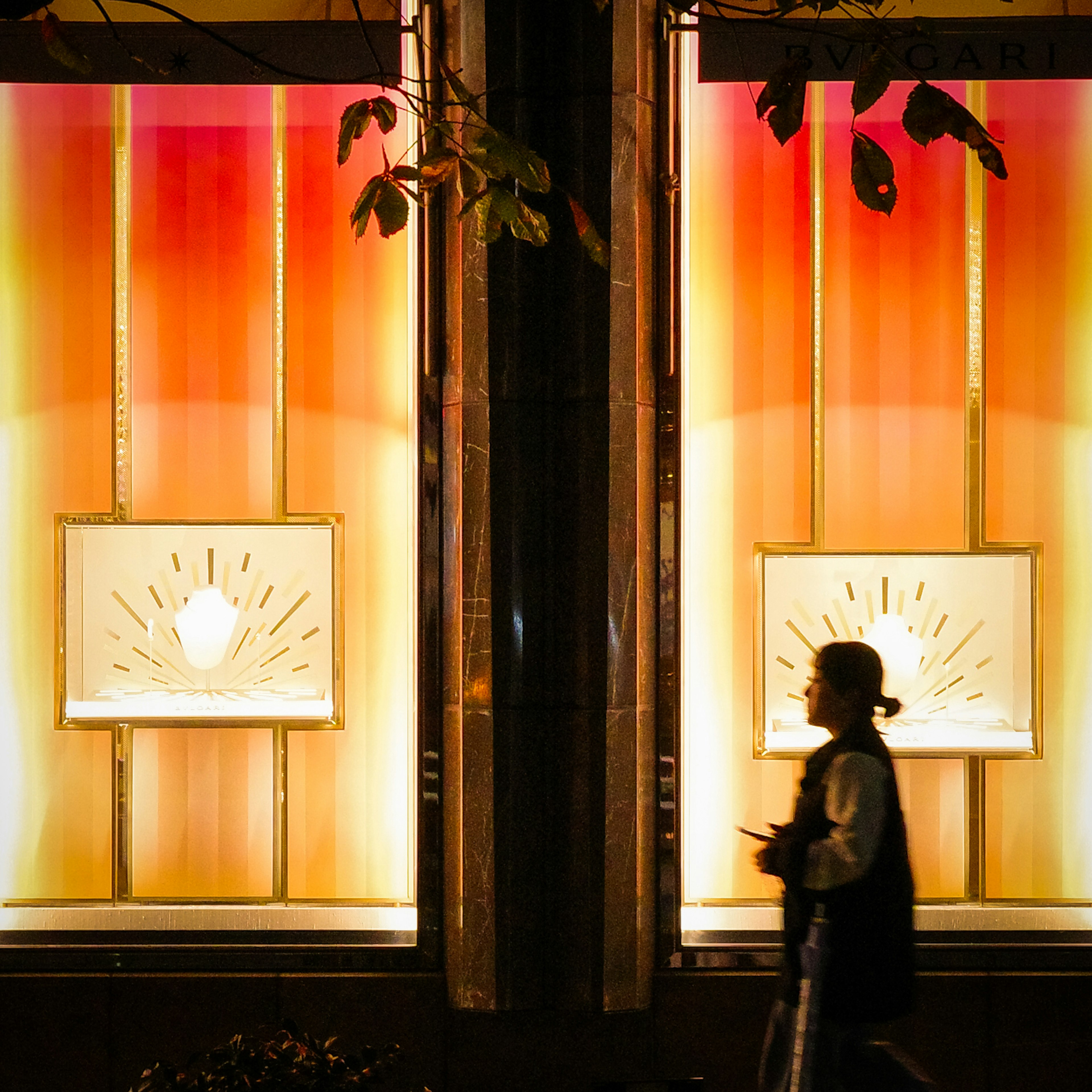 Silhouette d'une personne marchant devant des vitrines illuminées avec un éclairage dégradé orange