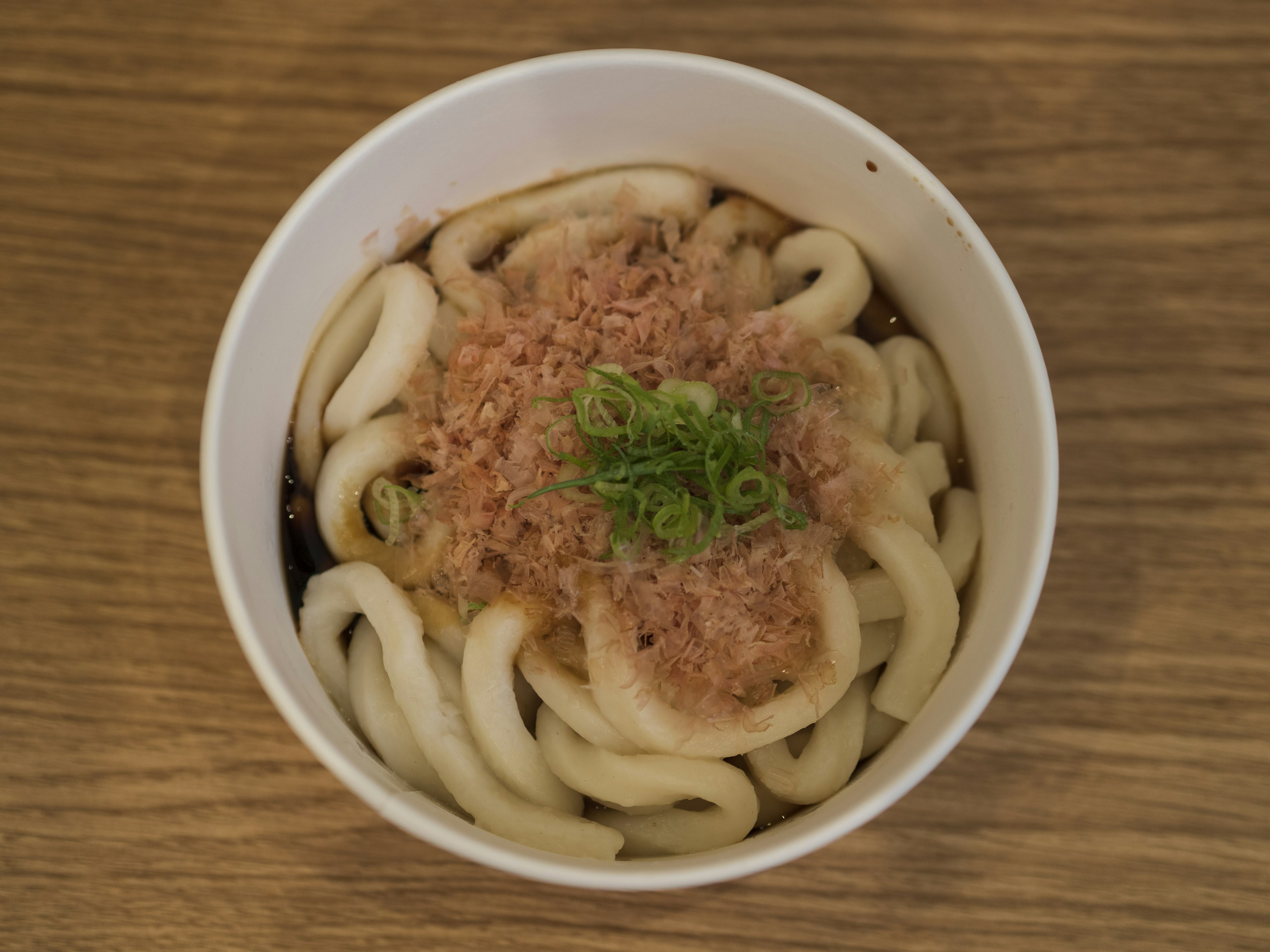 Fideos udon cubiertos con copos de bonito y cebollín en un tazón blanco