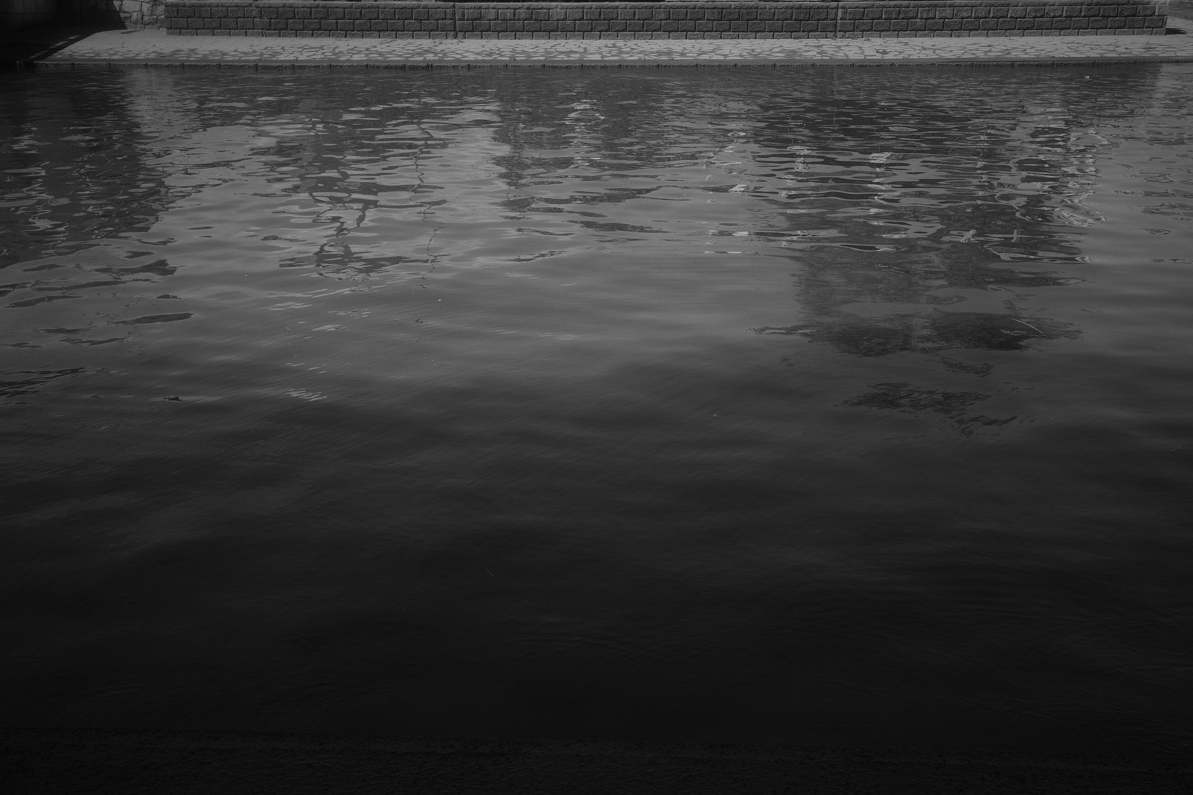 Monochrome image featuring reflections and ripples on the water surface