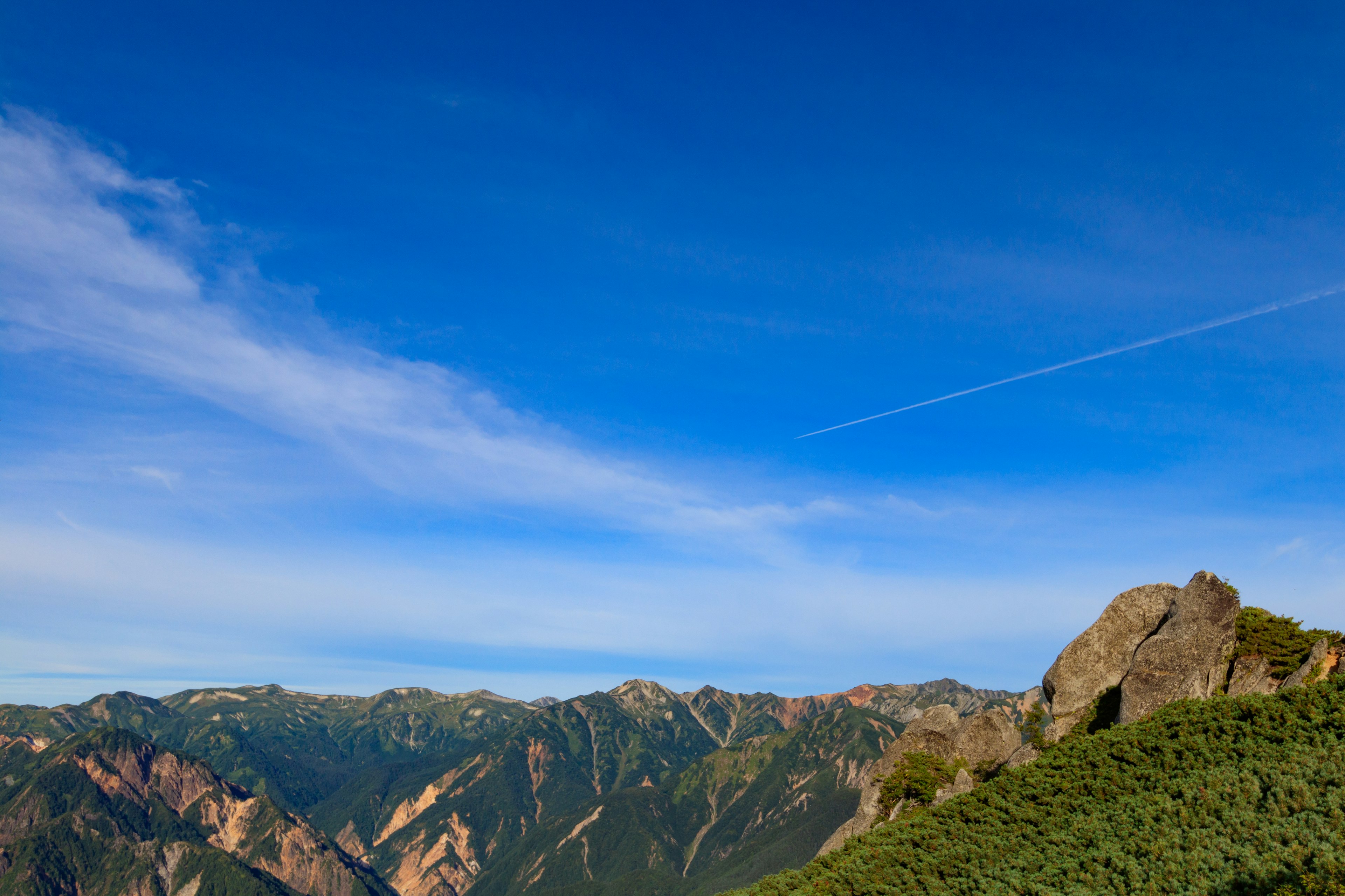 Vista escénica de montañas bajo un cielo azul claro con hierba verde y formaciones rocosas